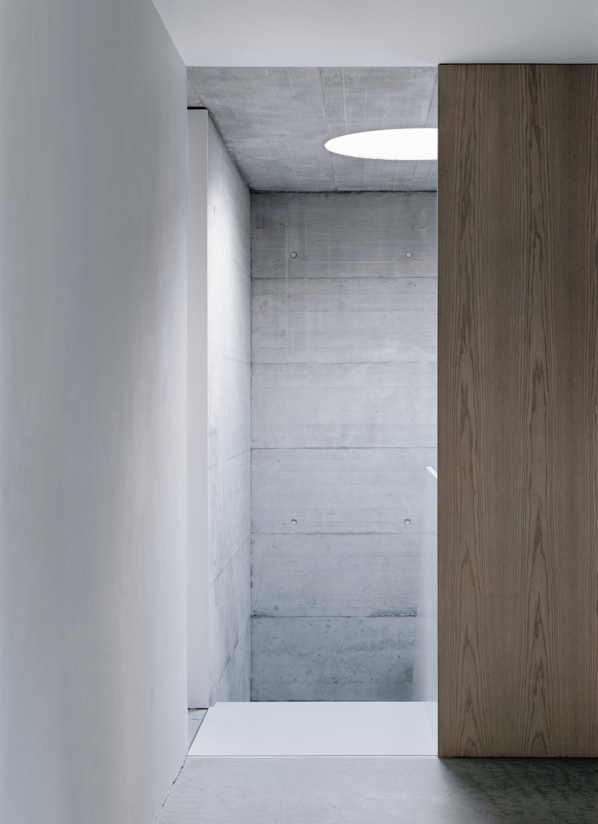 Corner detail showing board-formed concrete walls meeting white plaster beside a timber veneer cabinet
