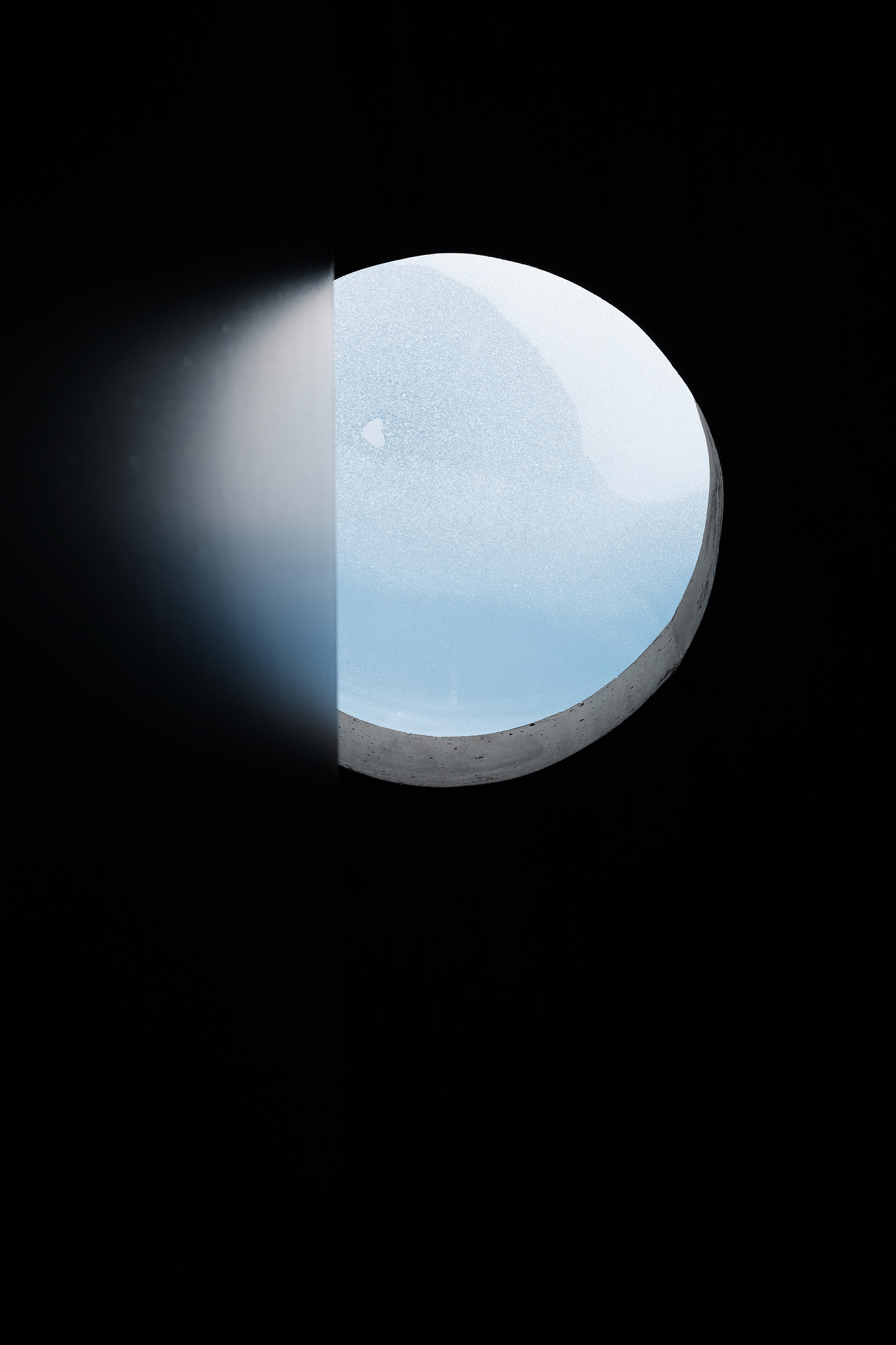 View through a circular concrete skylight opening showing snowfall against a pale grey sky