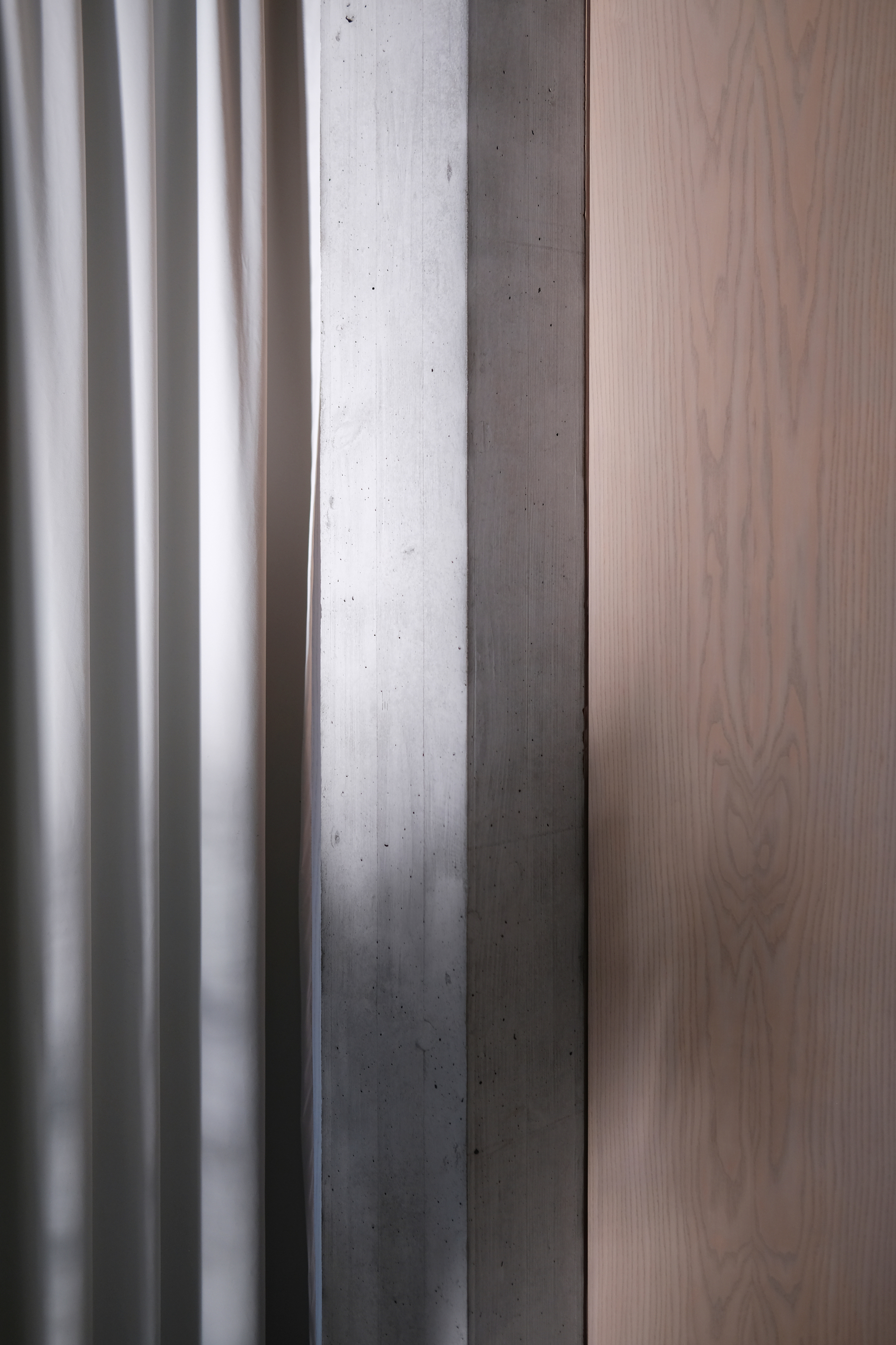 Close-up of white fluted paneling meeting exposed concrete column and pale wood veneer surface