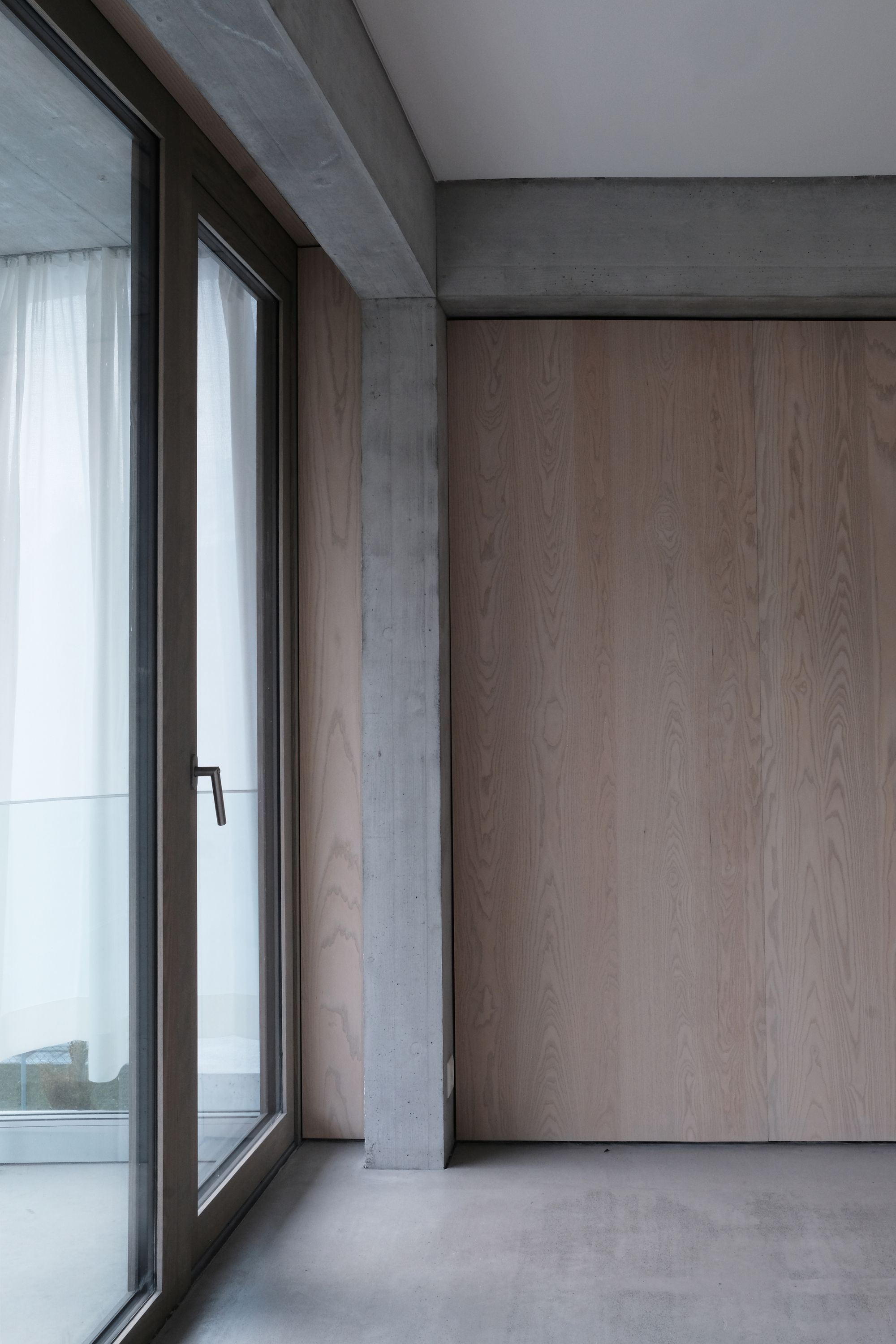 Corner window with black metal frame beside tall wood paneling and exposed concrete structure above