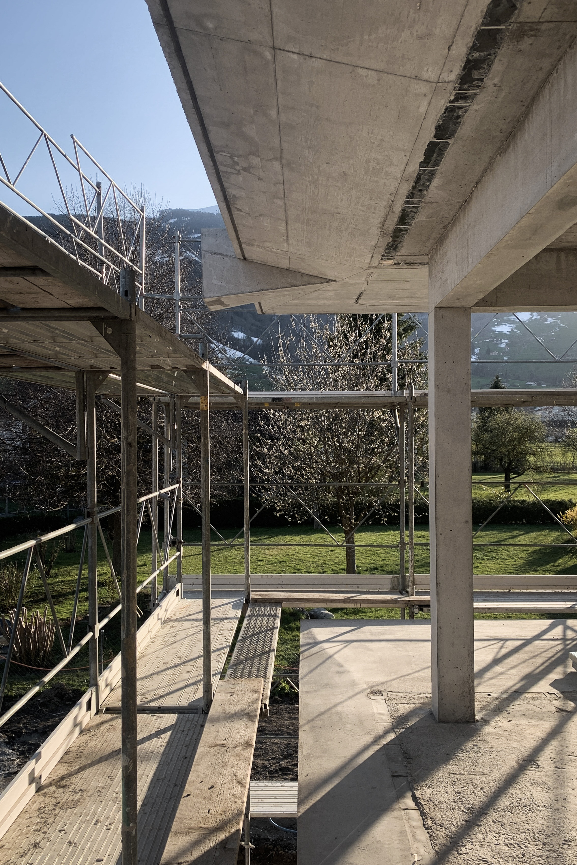 Underside of concrete slab with metal scaffolding and rectangular opening framing garden and trees beyond