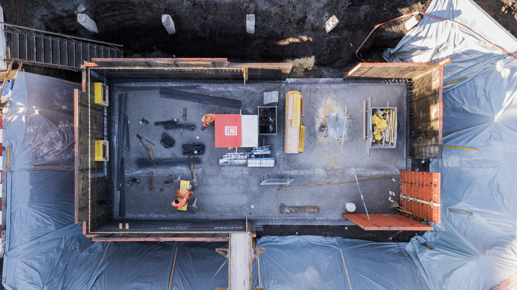 Overhead view of concrete slab during construction with workers and protective tarps