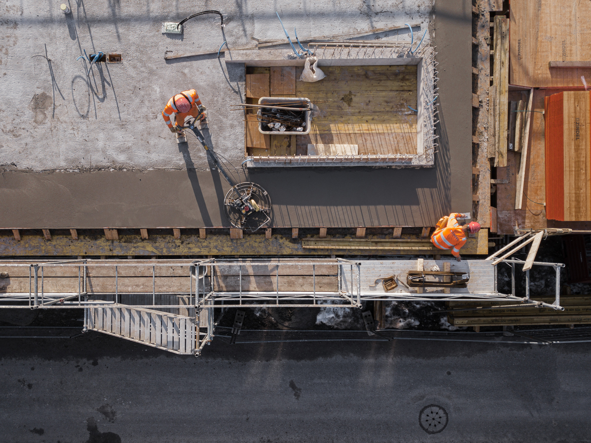 Drone view of construction workers positioning a timber-framed module beside fresh concrete slab