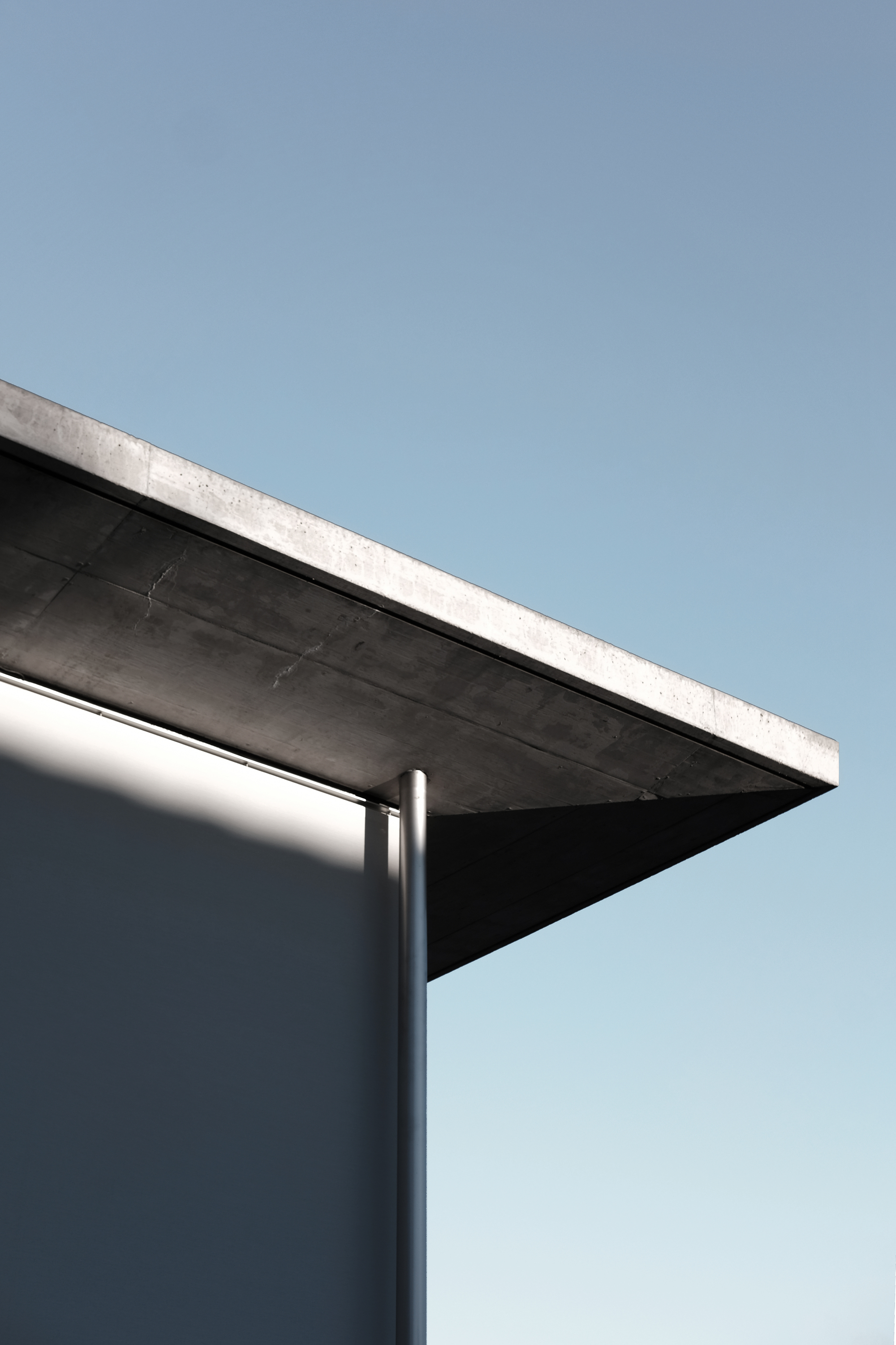 Corner detail of concrete roof slab cantilevering over cylindrical steel column against clear sky