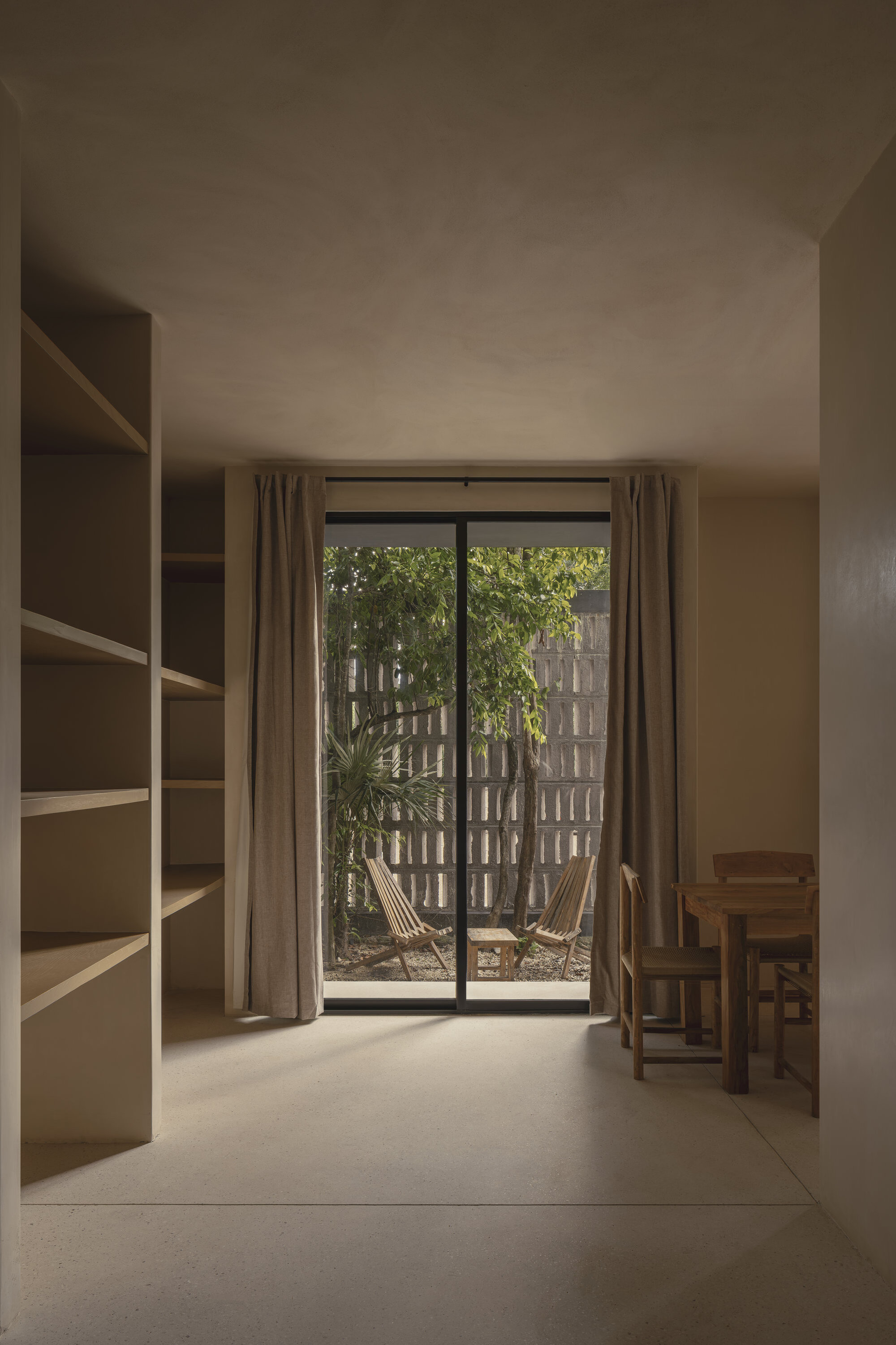 Interior room with built-in shelving and glazed doors opening to planted courtyard with block screen wall