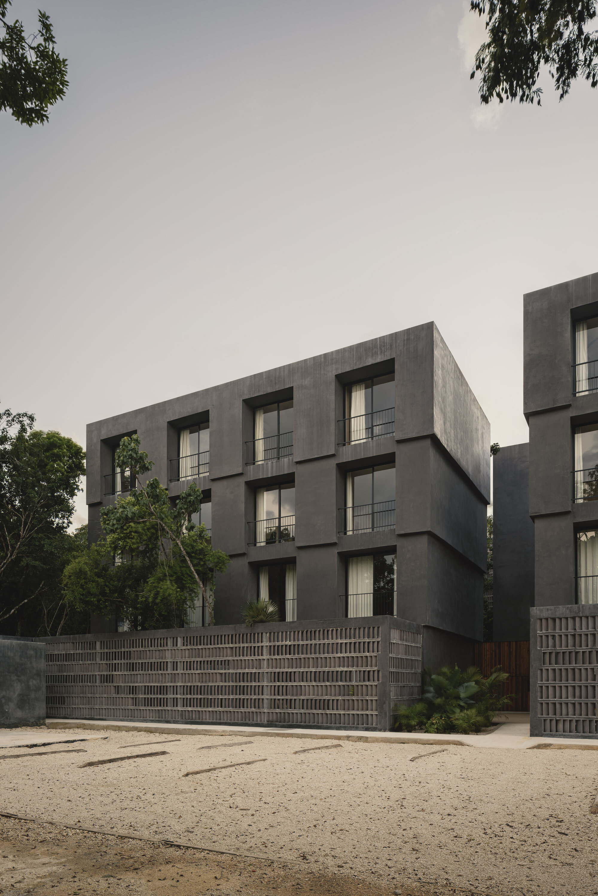 Street view of the concrete block facade with recessed balconies framed by trees under an overcast sky