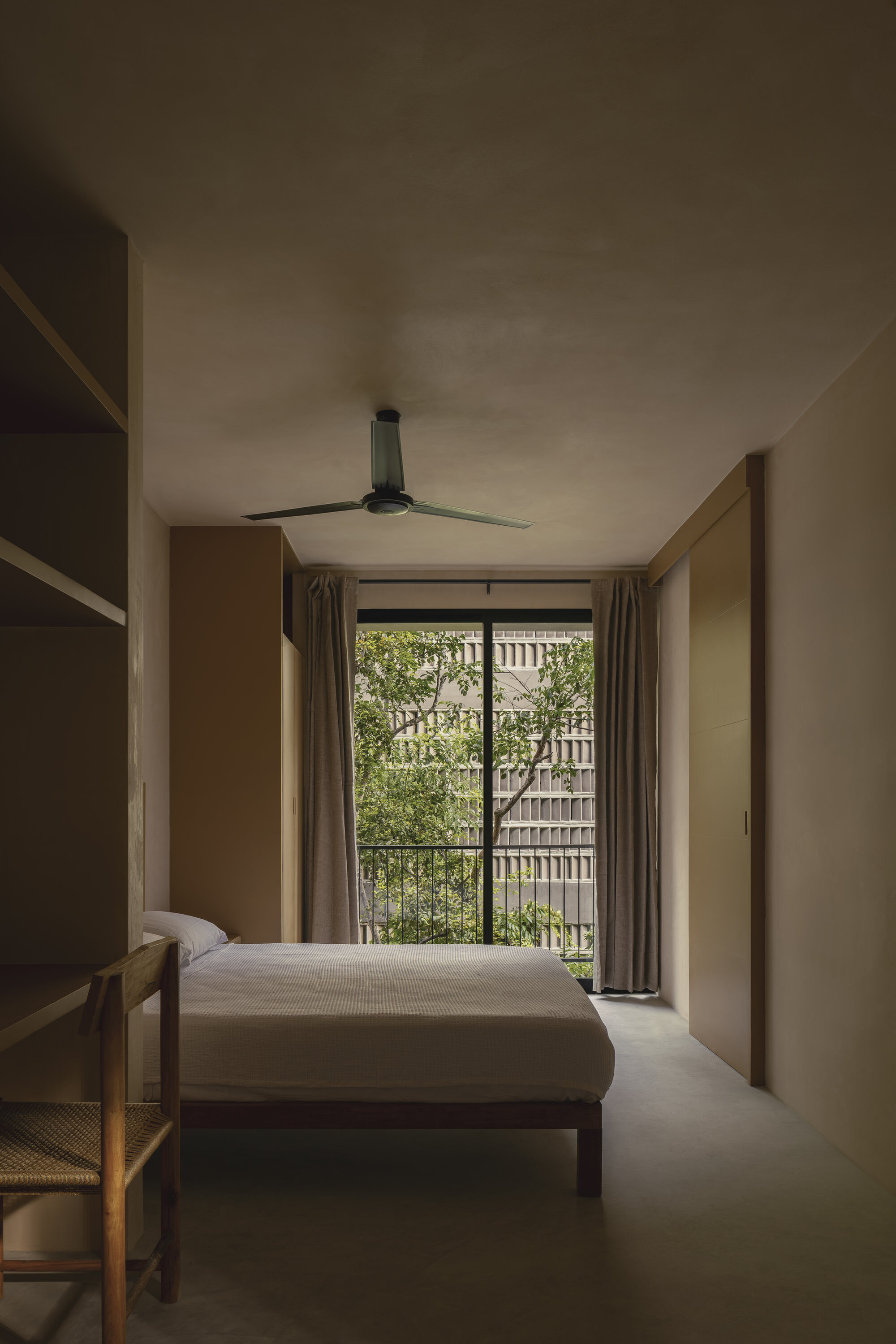 Bedroom with timber bed and ceiling fan facing a glazed door overlooking the perforated screen courtyard