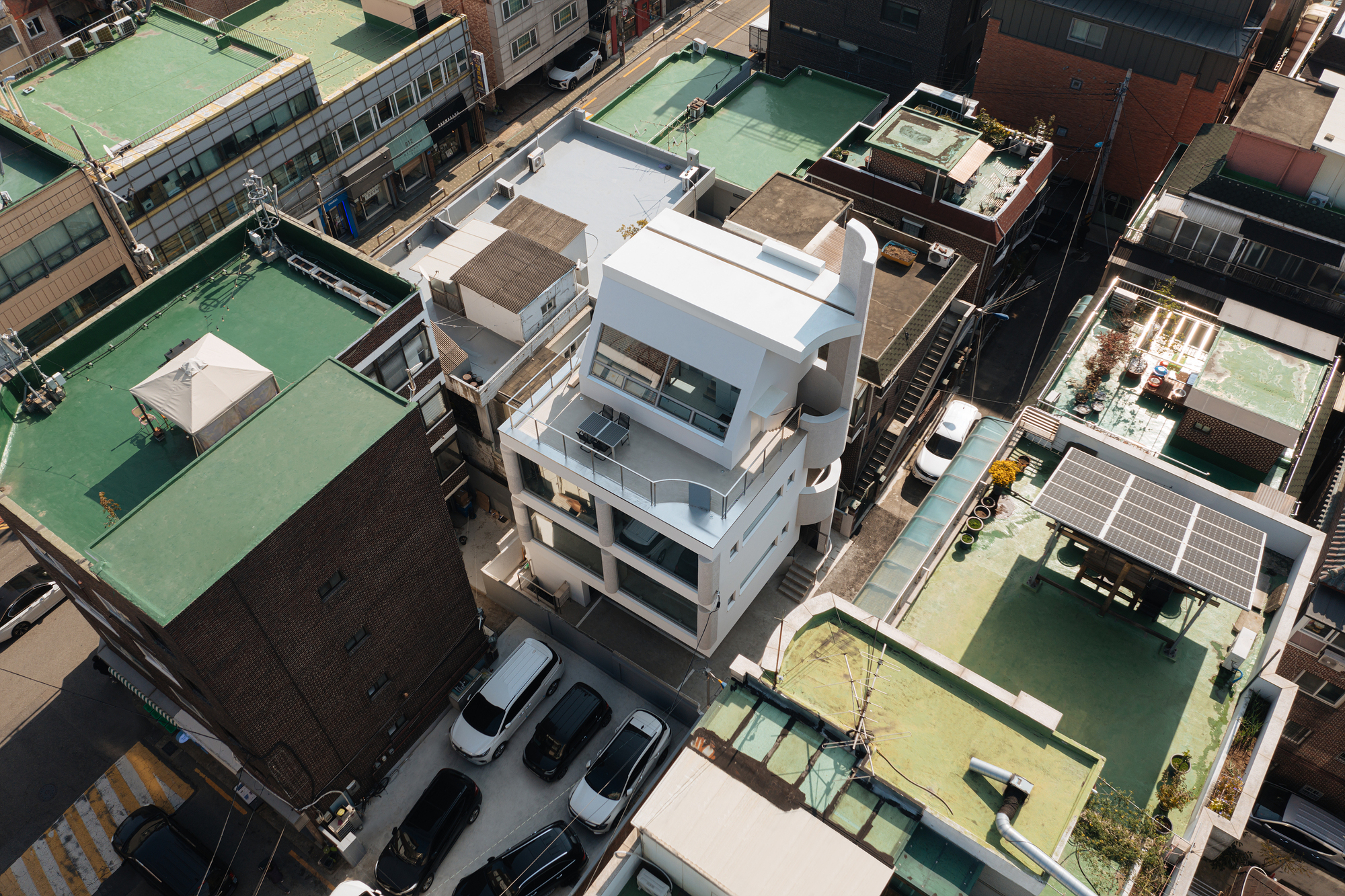 Aerial view of a white multi-story residence with rooftop terraces among densely packed neighboring buildings