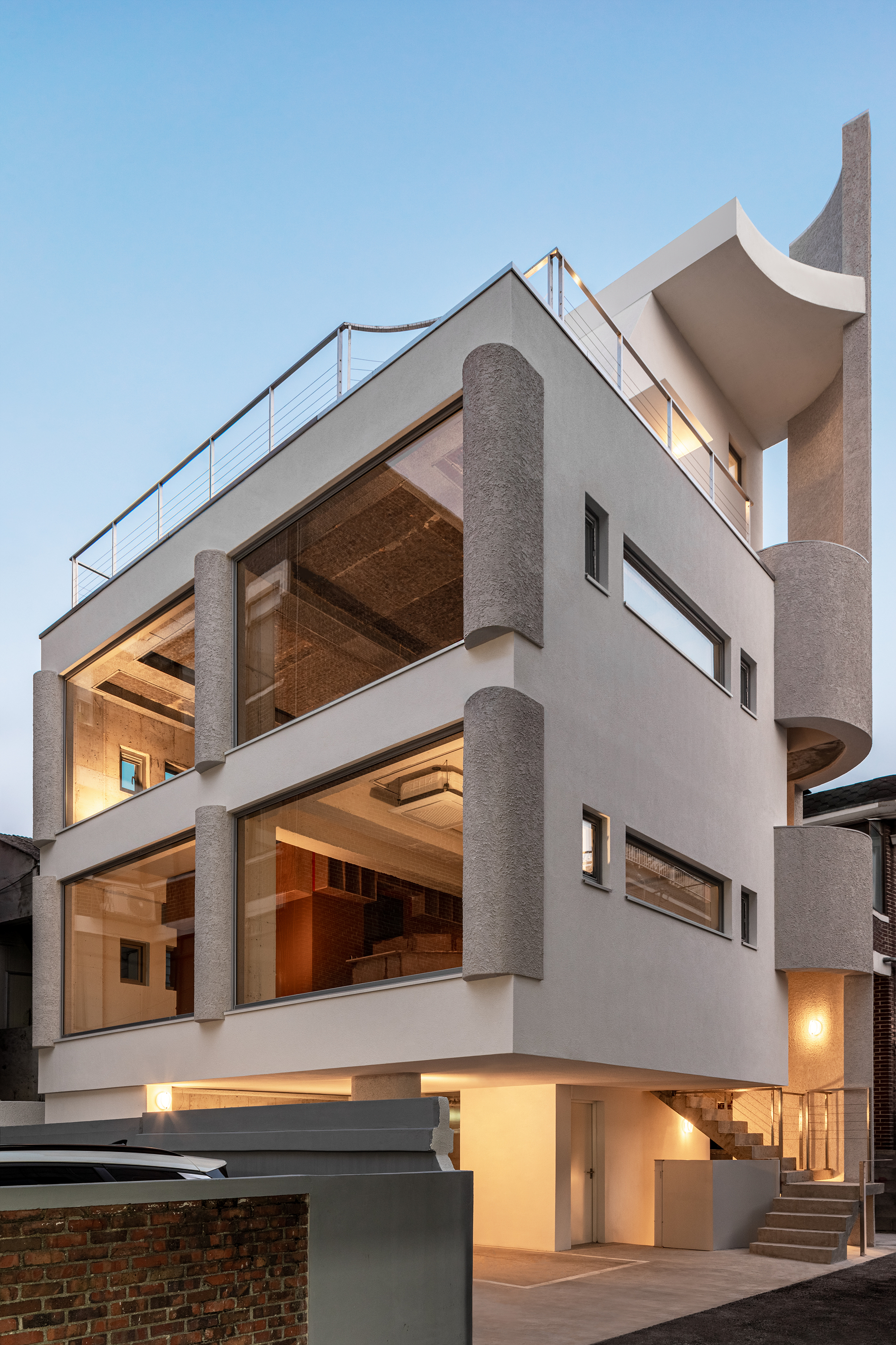 White rendered facade with cylindrical columns and exposed timber ceilings illuminated at dusk