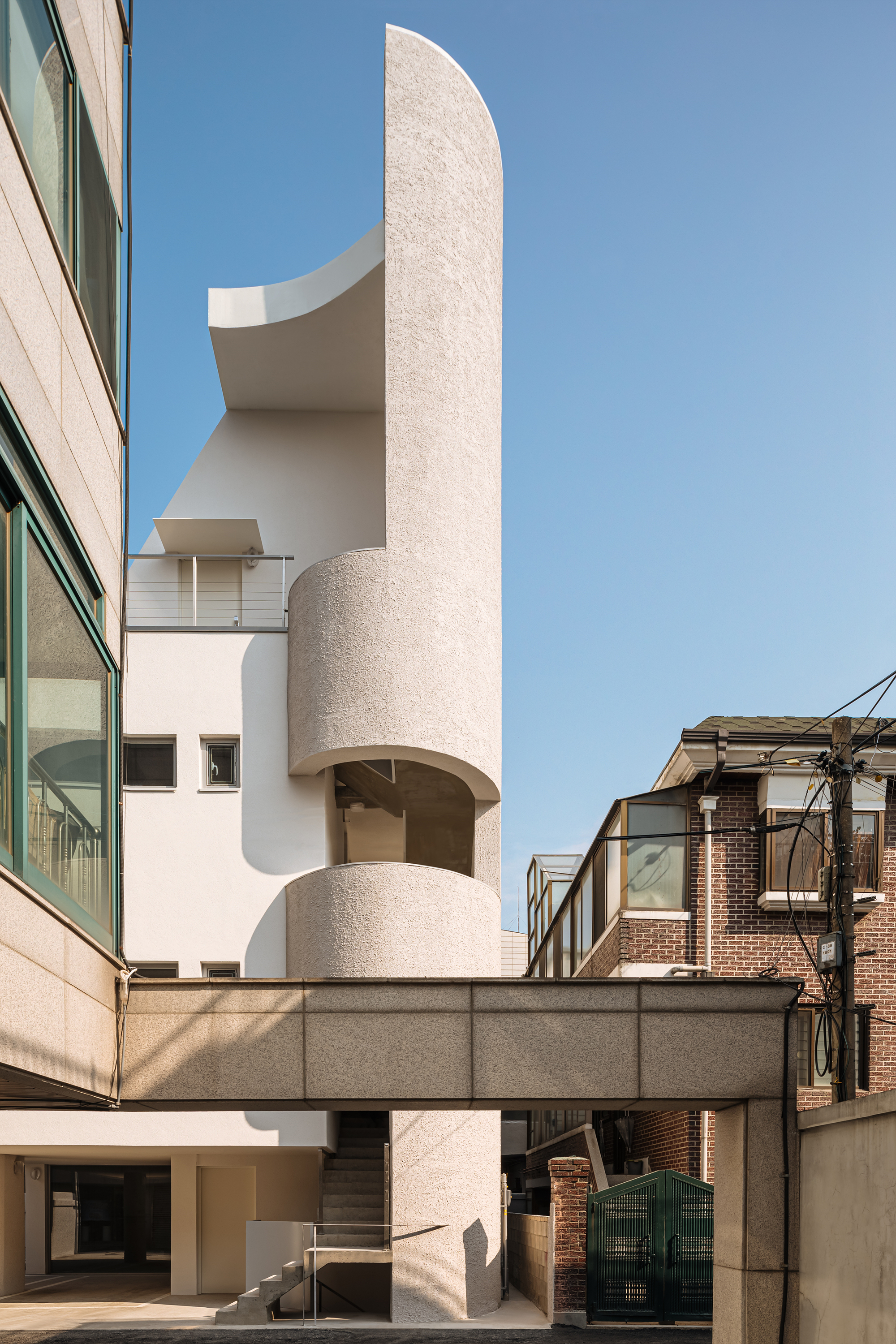 Curved cylindrical tower element with textured plaster finish rising above a horizontal concrete bridge
