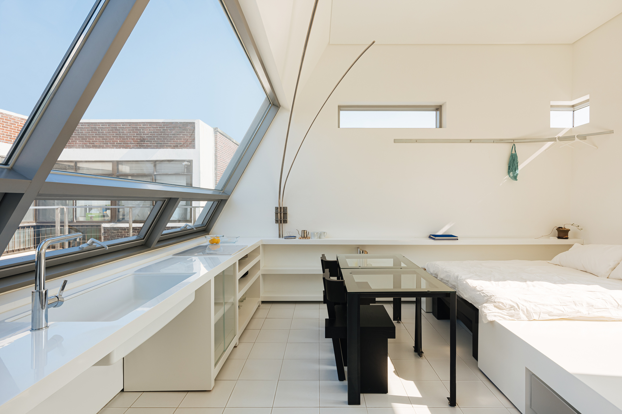 Open studio space with angled glazing, white tile floor and built-in counter under skylight