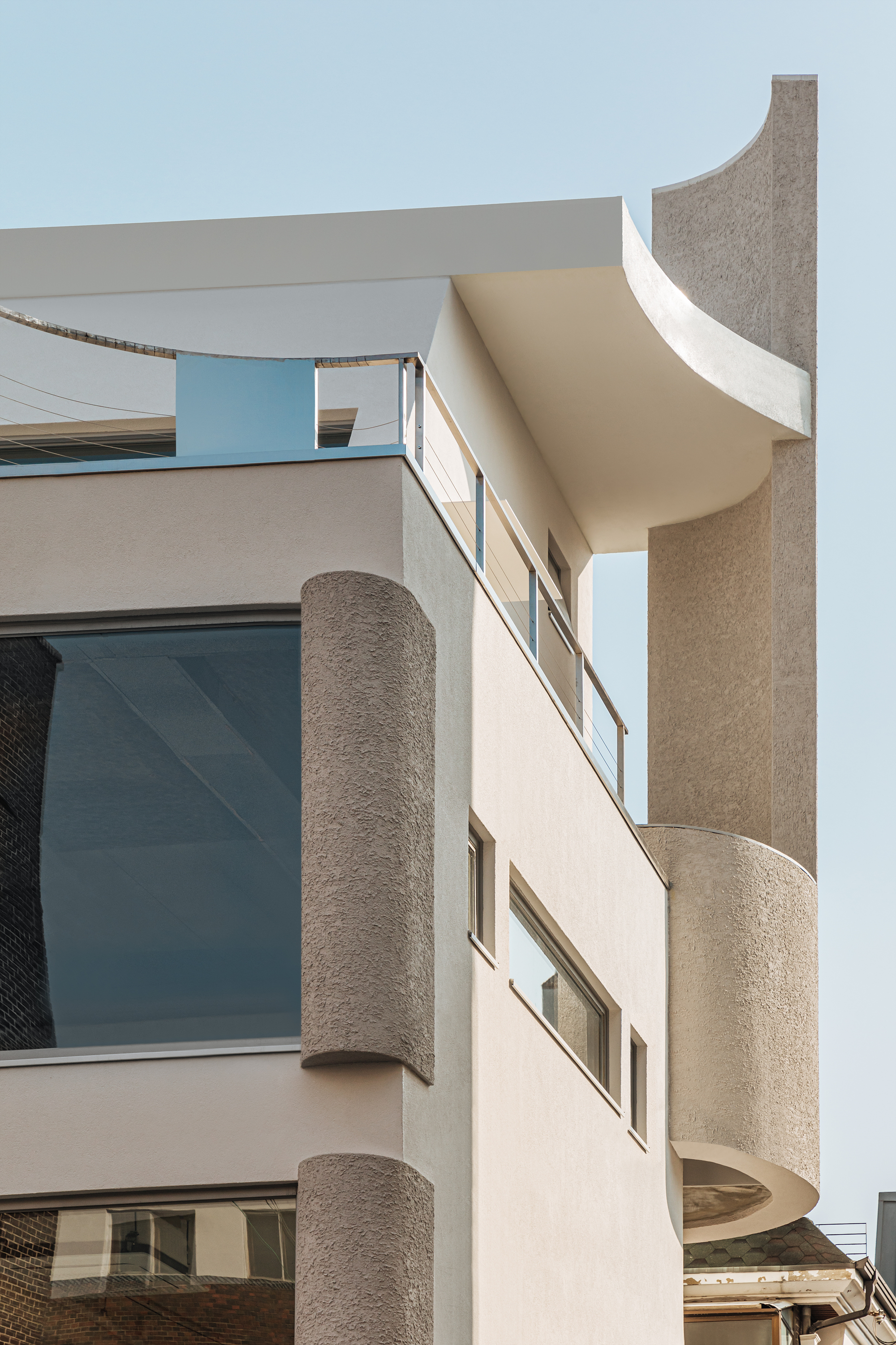 Textured cylindrical columns and curved balconies framing horizontal window openings under a clear sky