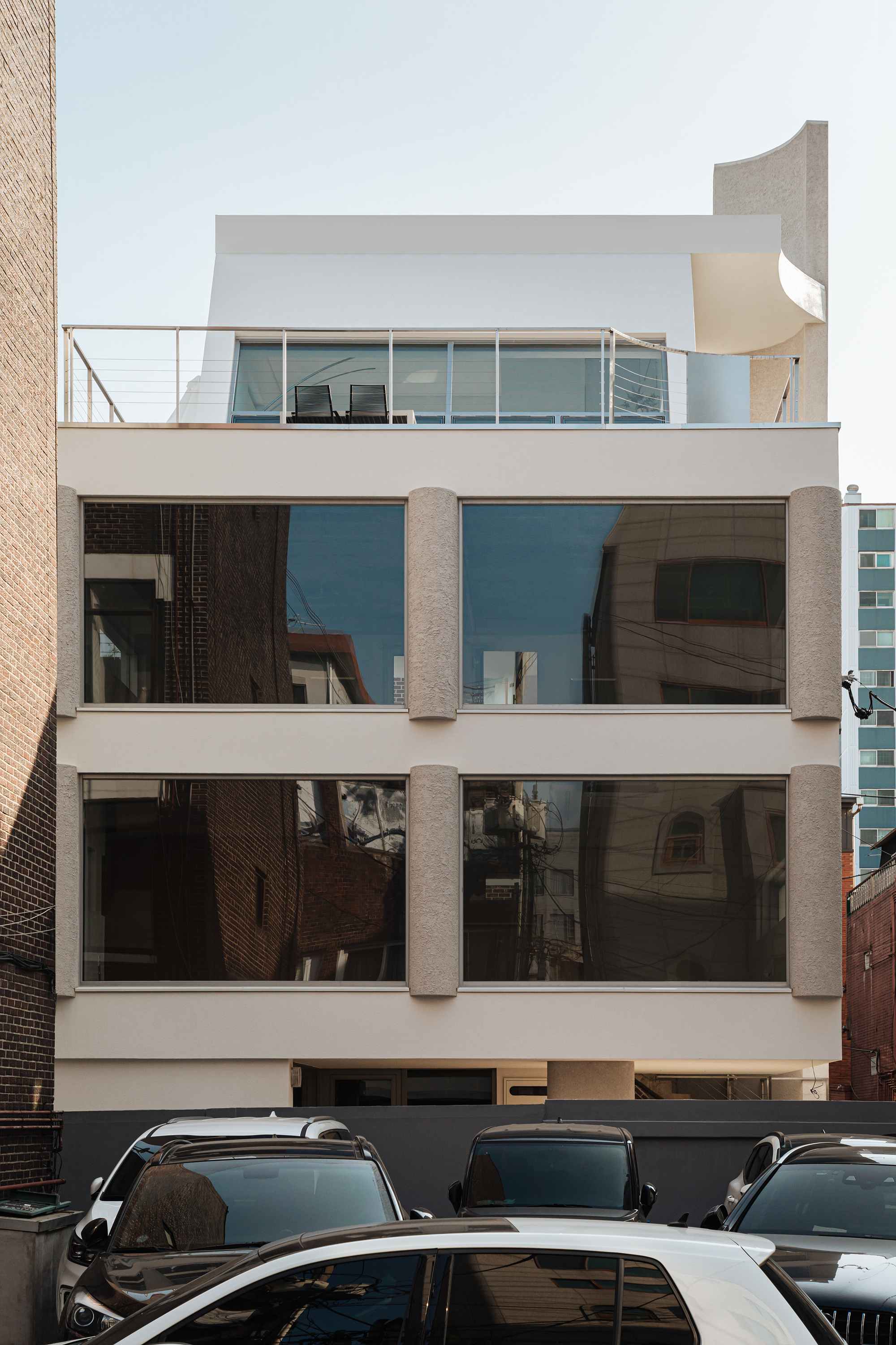 Street facade showing stacked balconies with floor-to-ceiling glazing and textured vertical columns between parked cars
