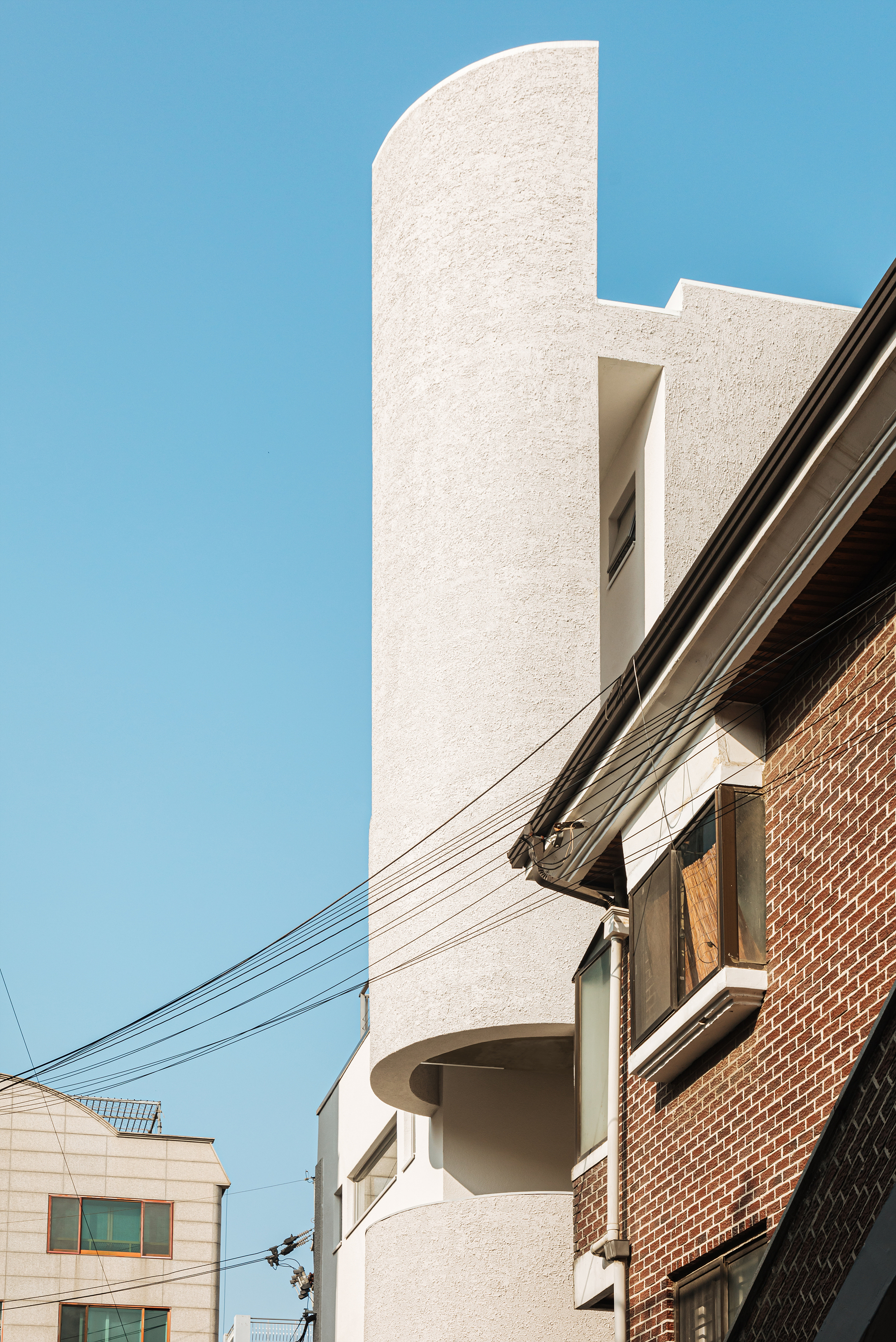 Curved textured tower rising above adjacent brick structure with overhead power lines against blue sky