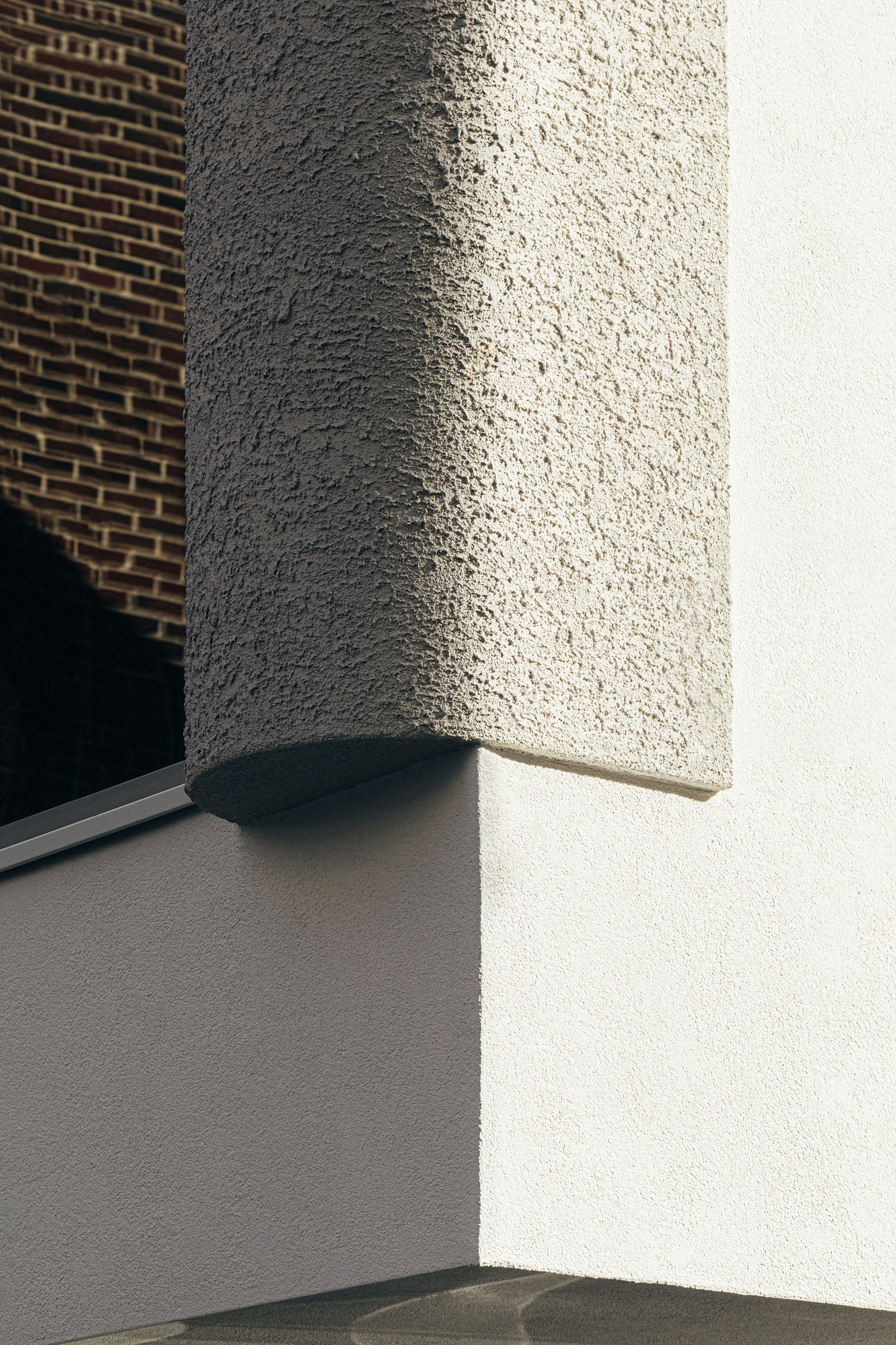 Close-up of textured stucco corner pillar with angled sunlight against adjacent brick wall