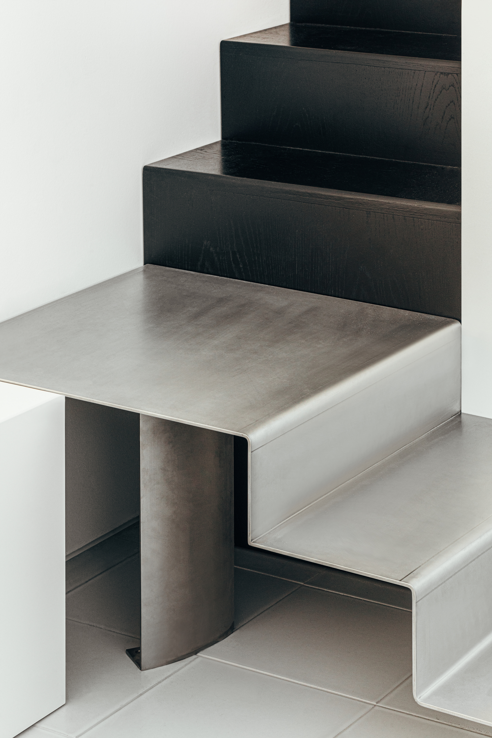 Detail of folded metal stair treads meeting black timber risers in a white interior