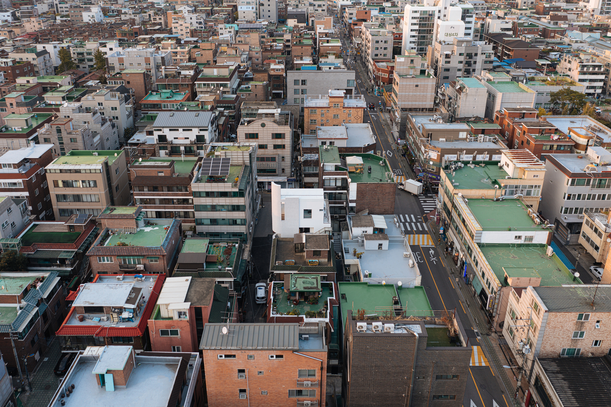 Aerial view of dense low-rise rooftops with green metal cladding and streets between mixed-use blocks