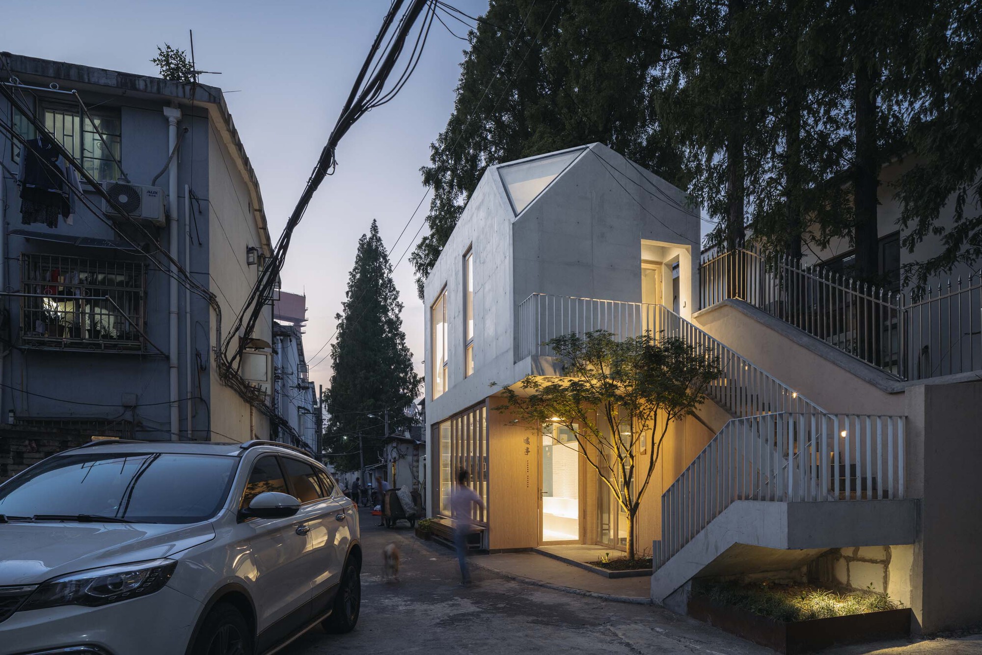 Street view of the white concrete house with vertical slatted screens and an illuminated tree at dusk