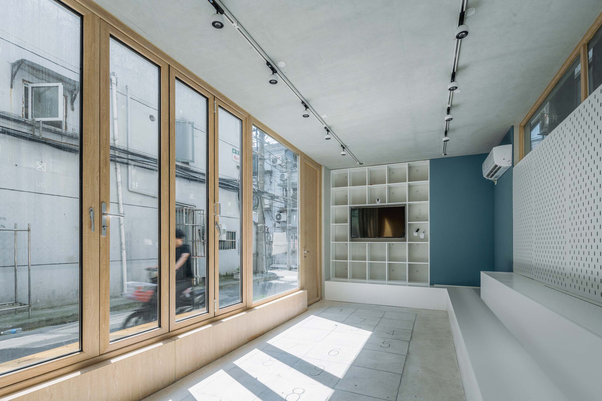 Interior space with timber-framed glazing, white grid shelving and track lighting on the concrete ceiling