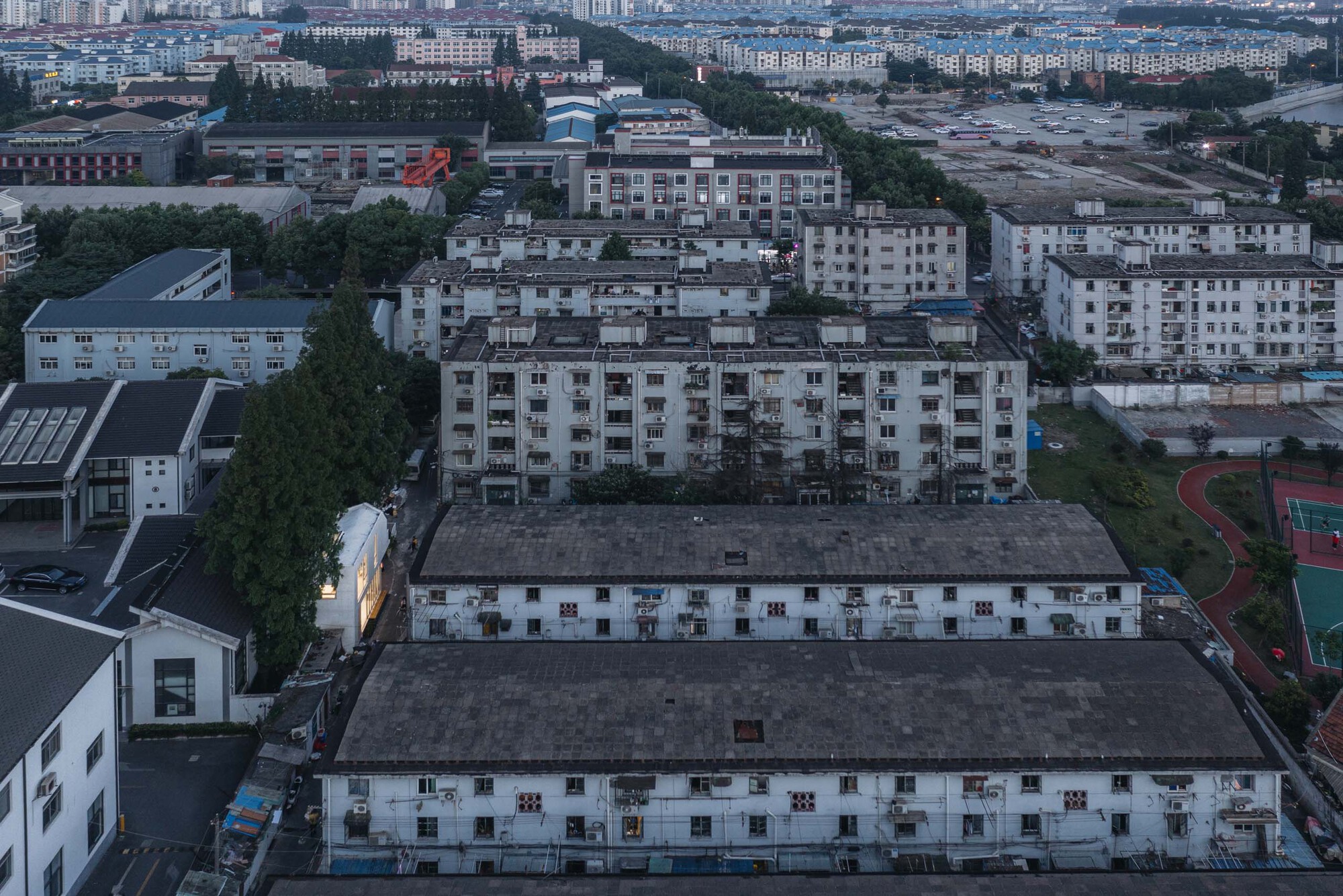 Drone view of the illuminated house nestled between residential blocks and a sports court at twilight