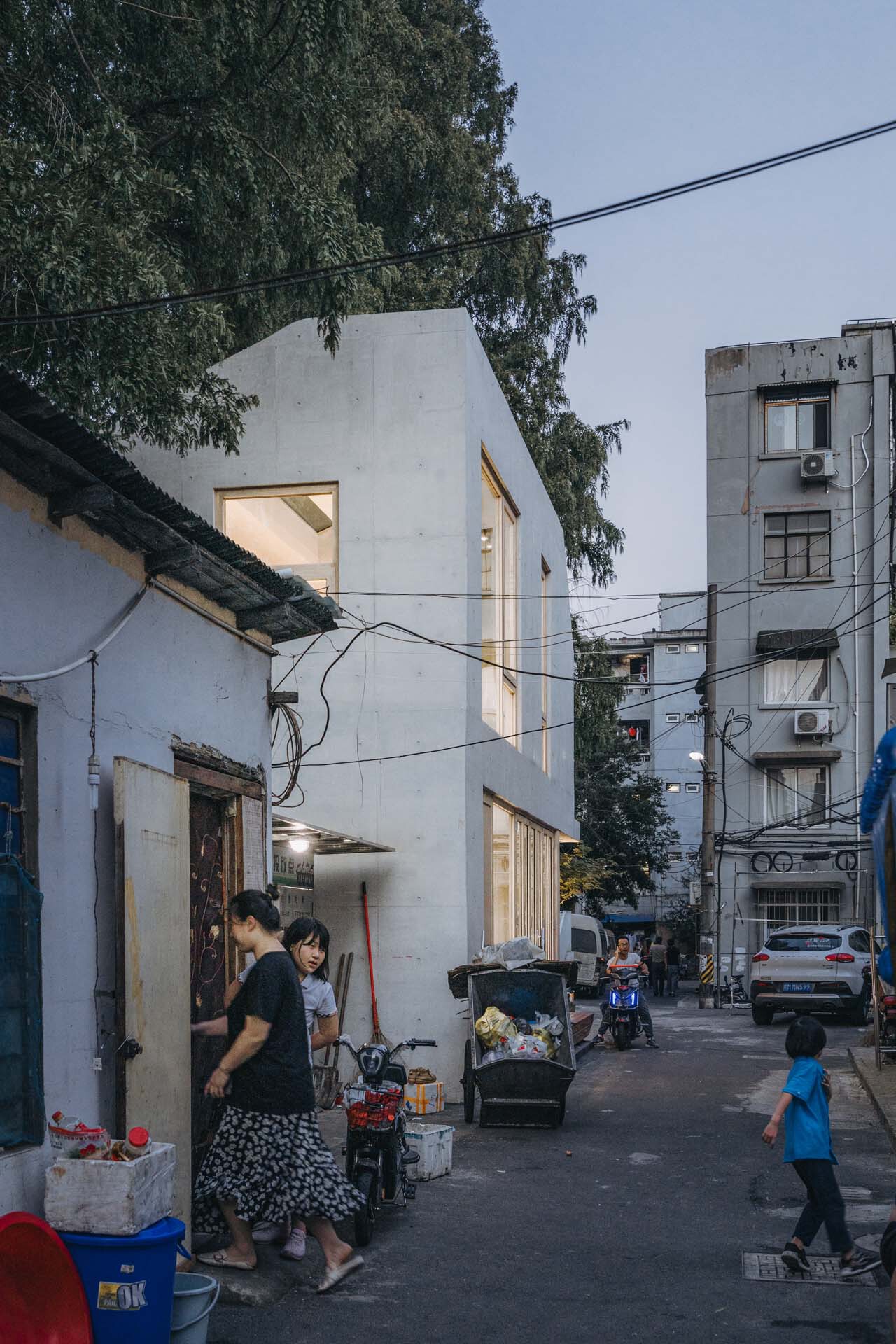 Street view of the angular white concrete insertion among traditional single-storey buildings at dusk