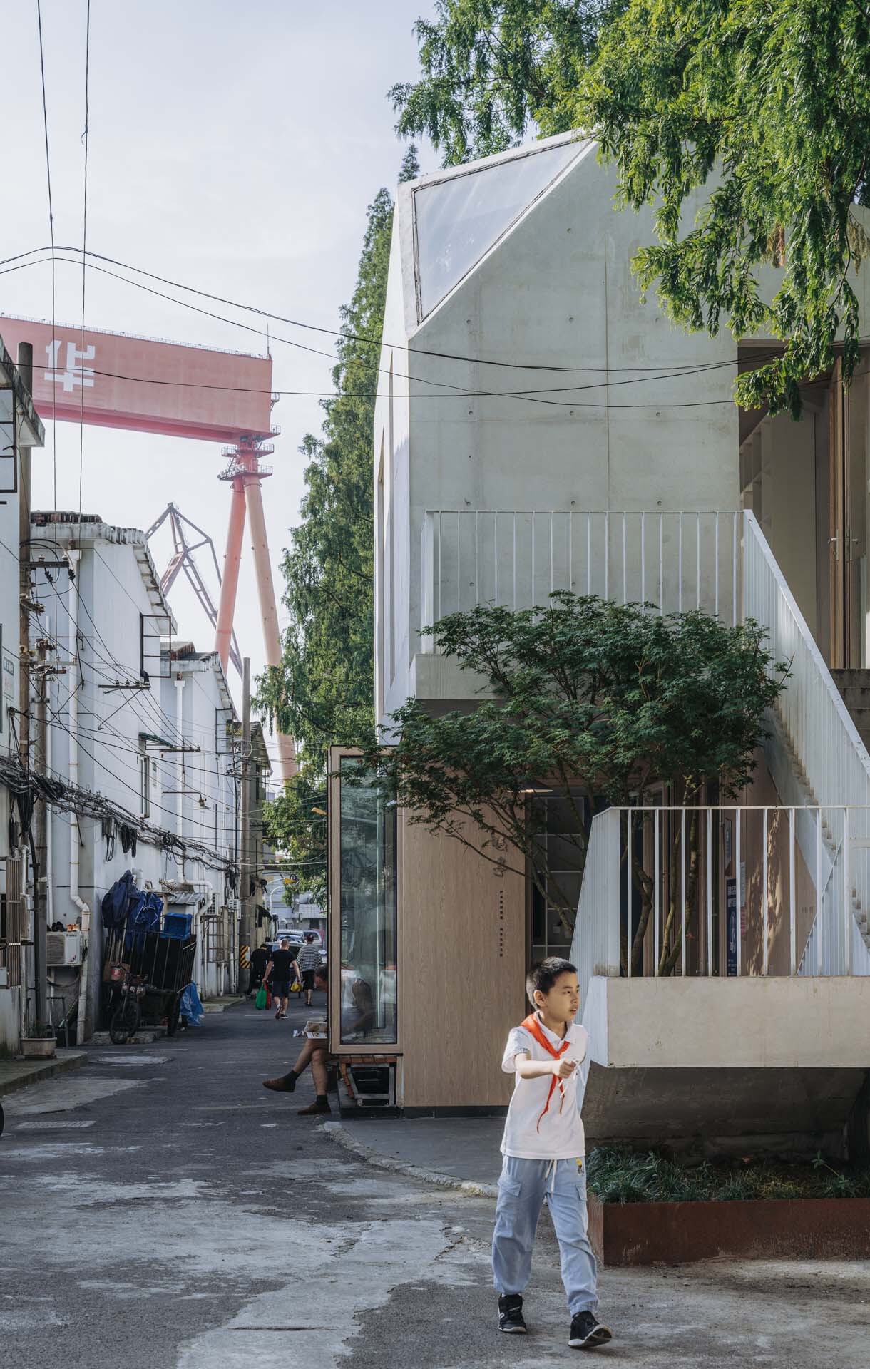 White concrete facade with folded planes and vertical slit window rising above a pedestrian in the alley