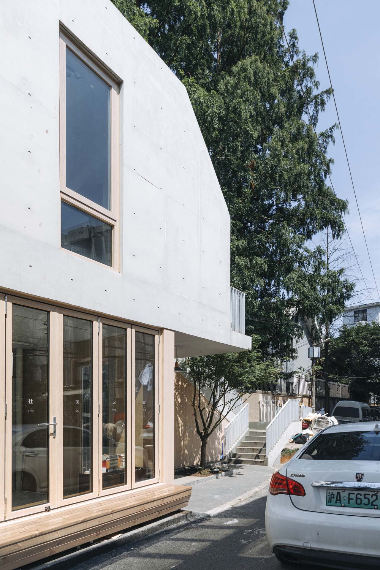 Corner detail showing the curved white concrete wall with tall windows and timber frames beside a parked car