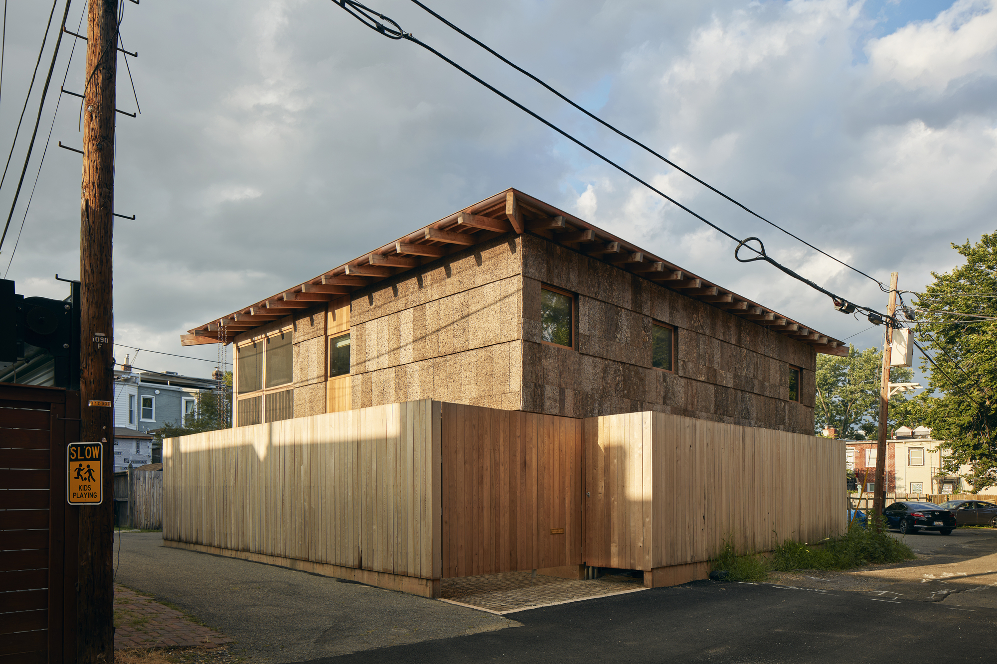 Street corner view of the two-story volume with exposed rafter tails and vertically clad timber fence below