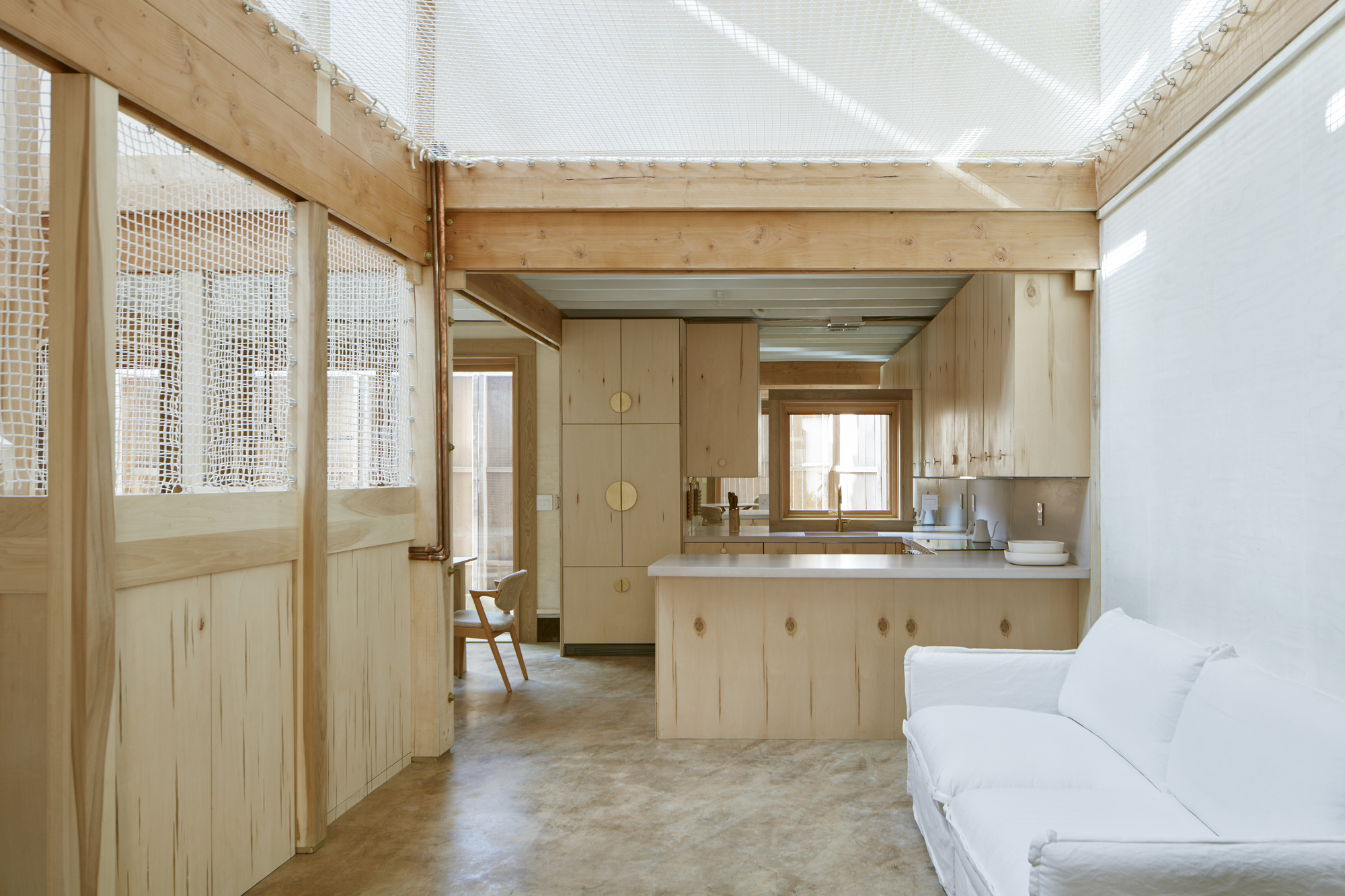 View through timber-framed mesh doors toward kitchen under a translucent skylight