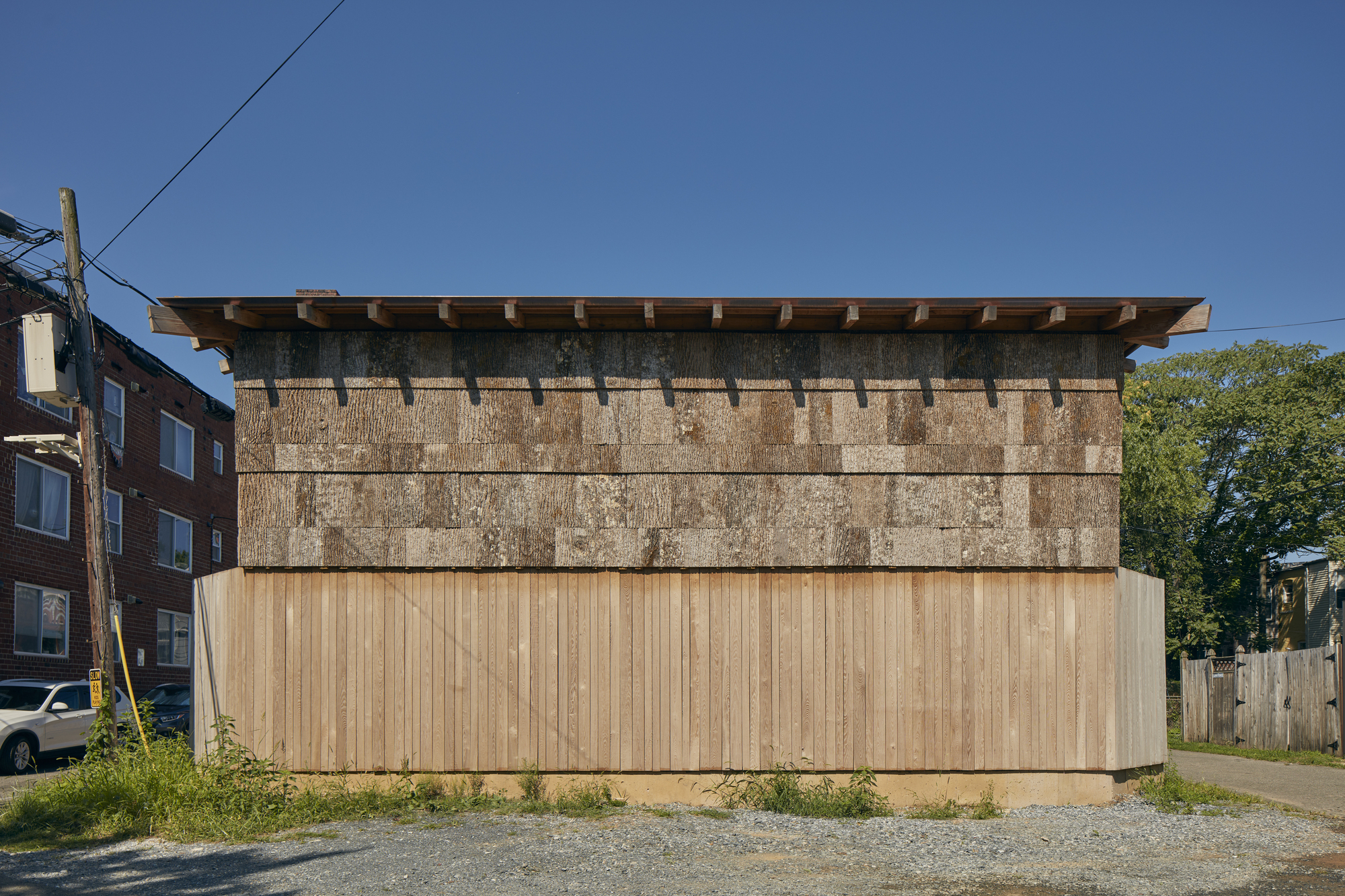 Street elevation showing the layered facade with vertical timber cladding below cast-stone panels and deep eaves