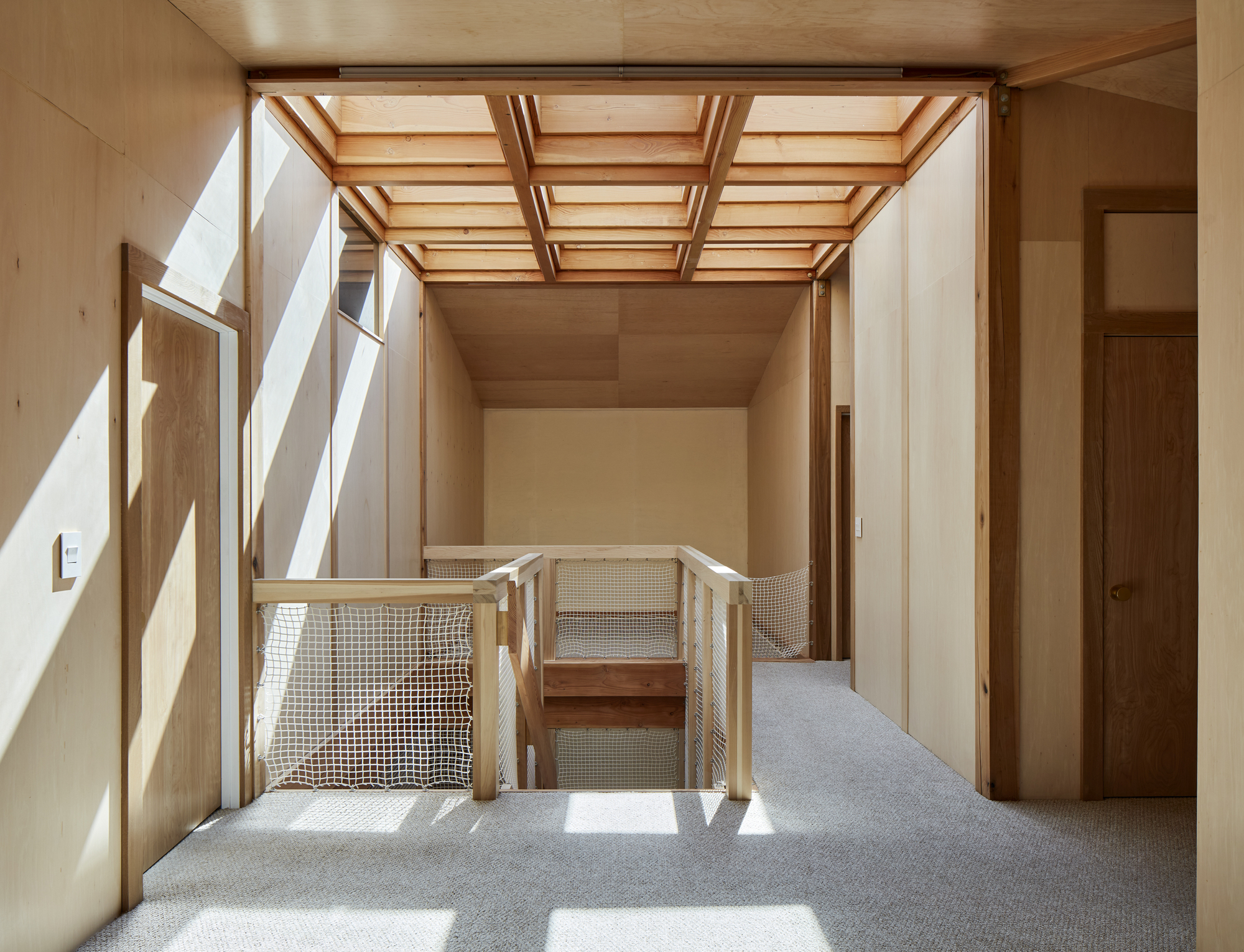 Interior landing with mesh balustrade and timber-framed skylight casting sunlight across carpeted floor