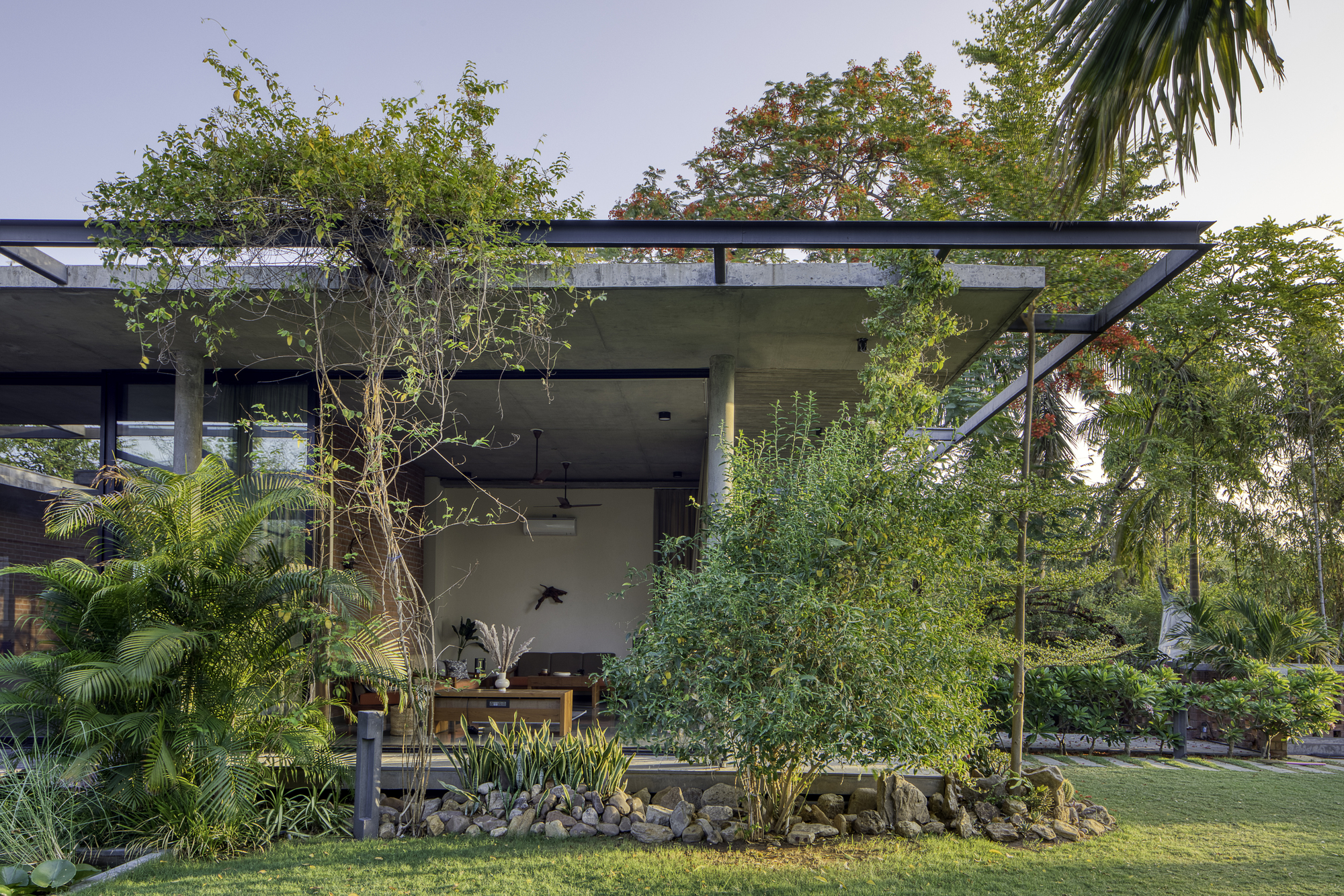 Covered outdoor pavilion with steel frame and concrete soffit surrounded by palm trees and tropical planting