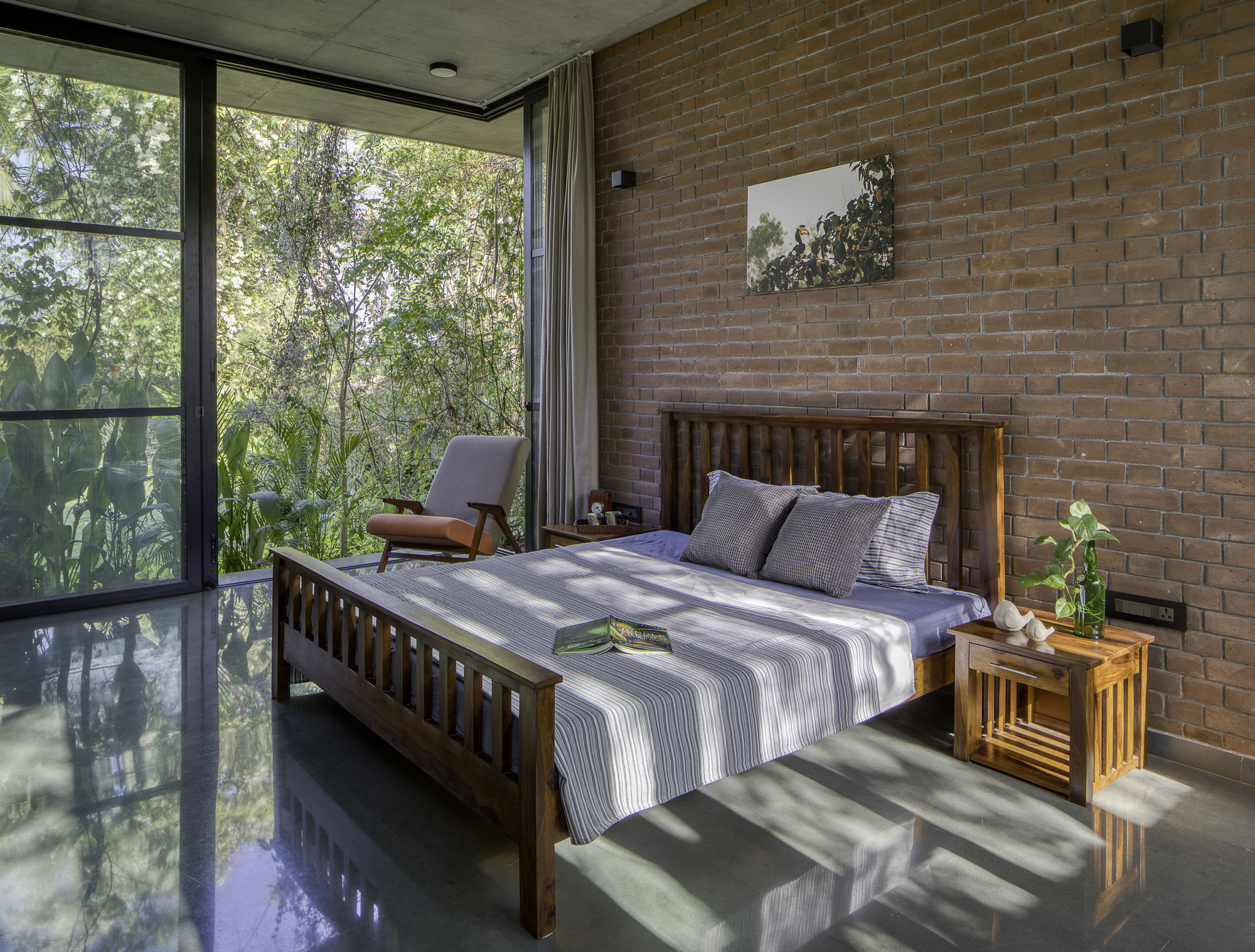 Bedroom with exposed brick wall and floor-to-ceiling glass overlooking garden with filtered morning light