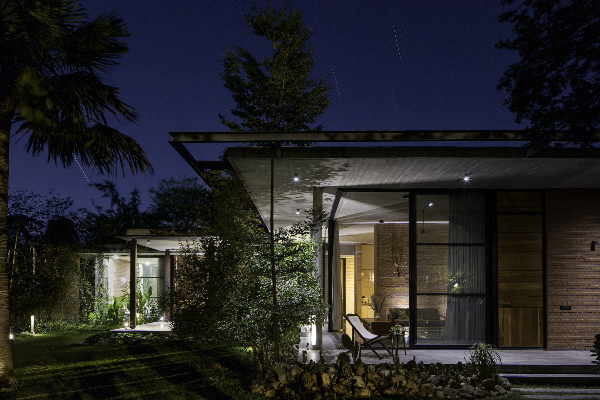 Garden view of the flat-roofed pavilion with floor-to-ceiling glazing and exposed concrete soffit at dusk