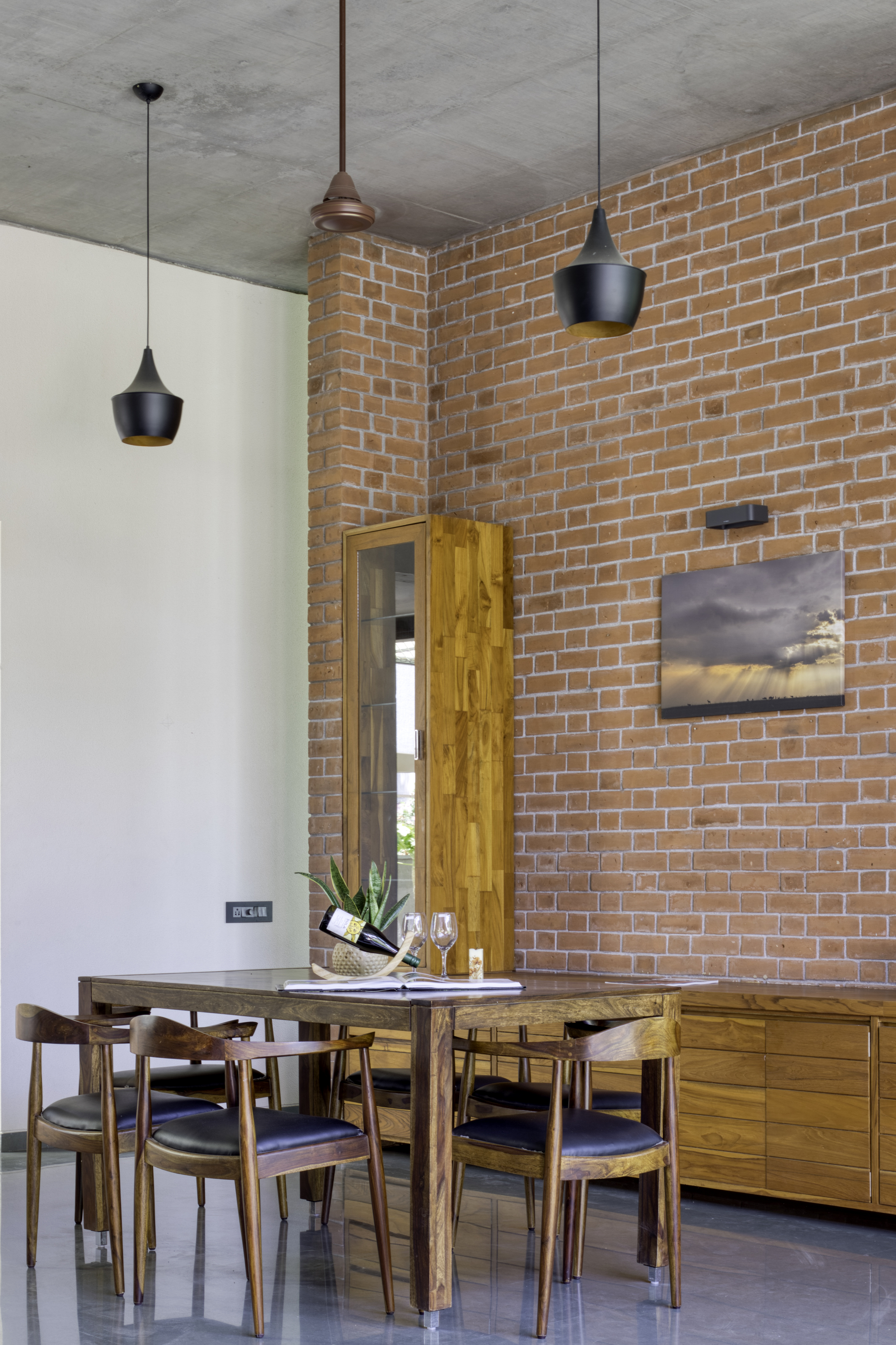 Dining area with exposed brick wall, concrete ceiling, black pendant lights, and timber furniture