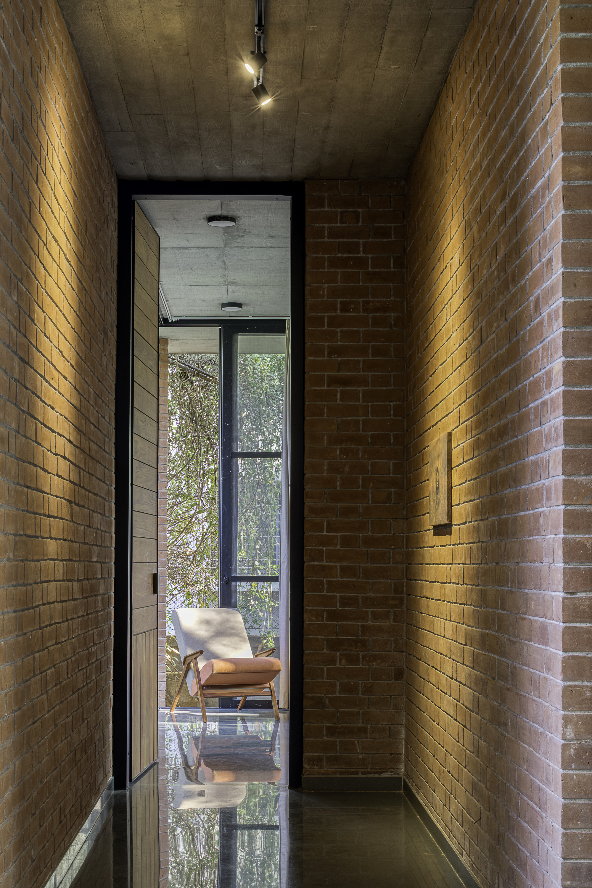 Narrow brick corridor with uplighting leading to a glazed threshold and concrete ceiling