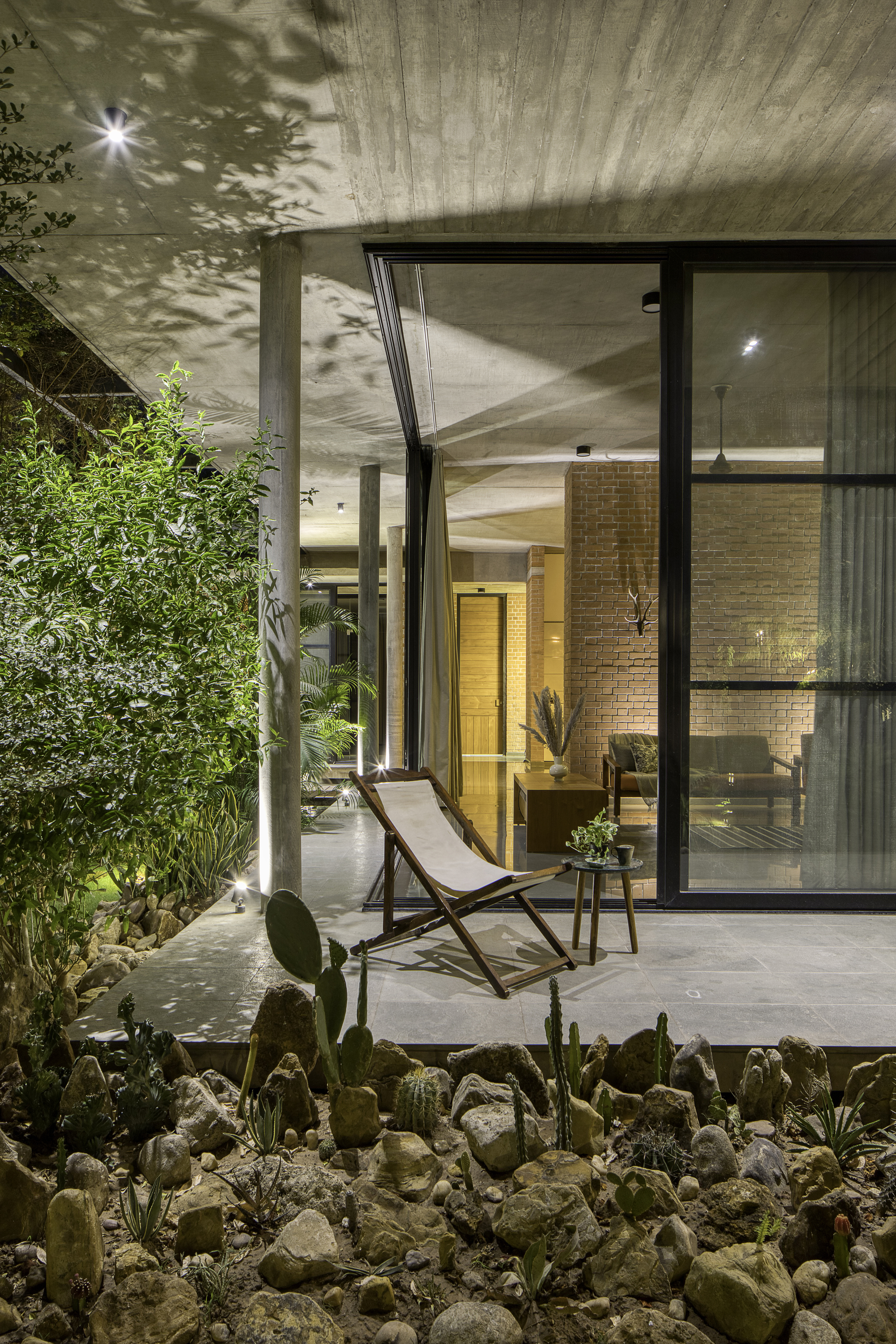 Courtyard terrace with planted cacti bed and lounge chair under concrete soffit at dusk