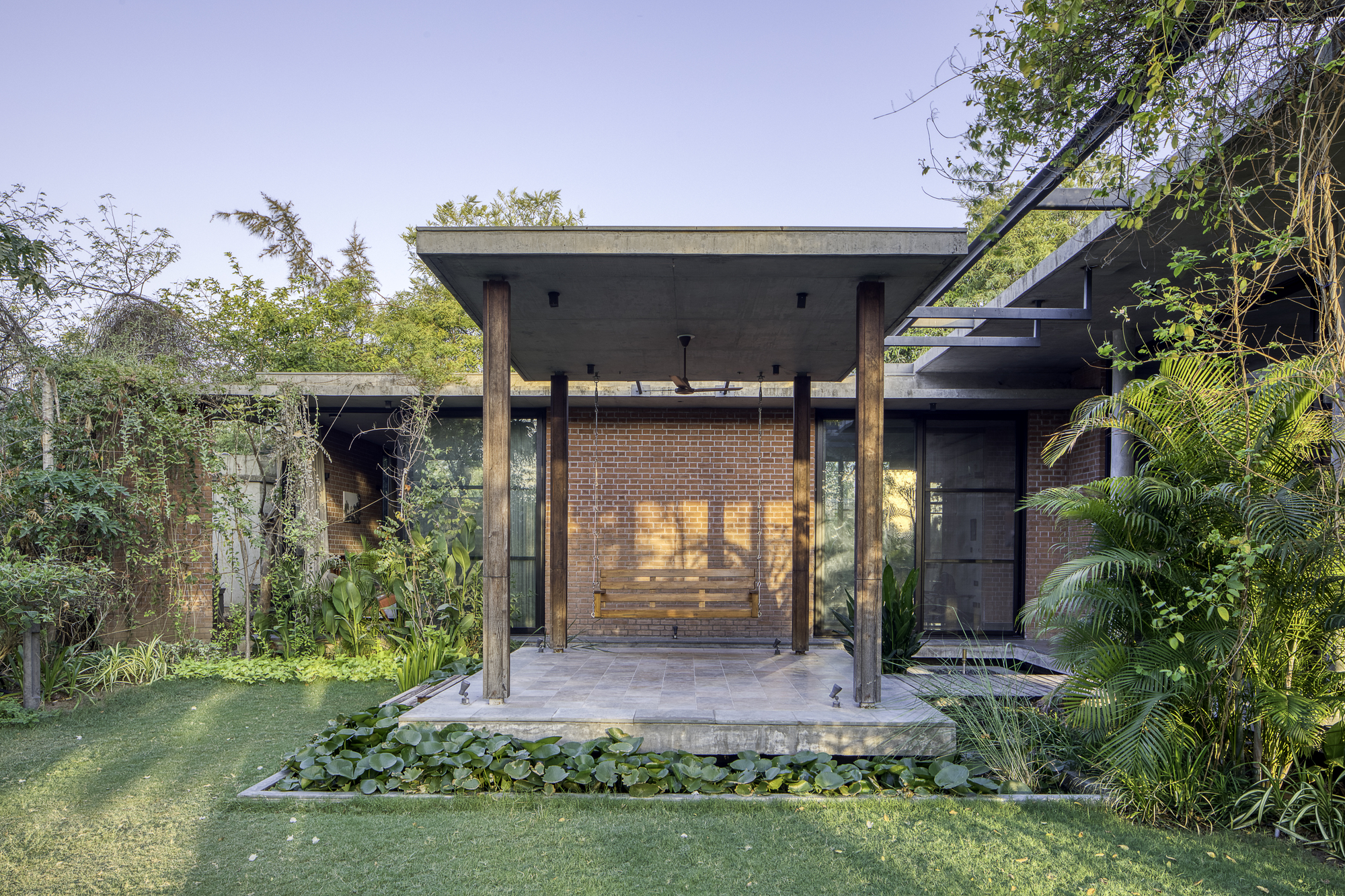 Entrance pavilion with timber columns and floating concrete roof framing a brick wall at dusk