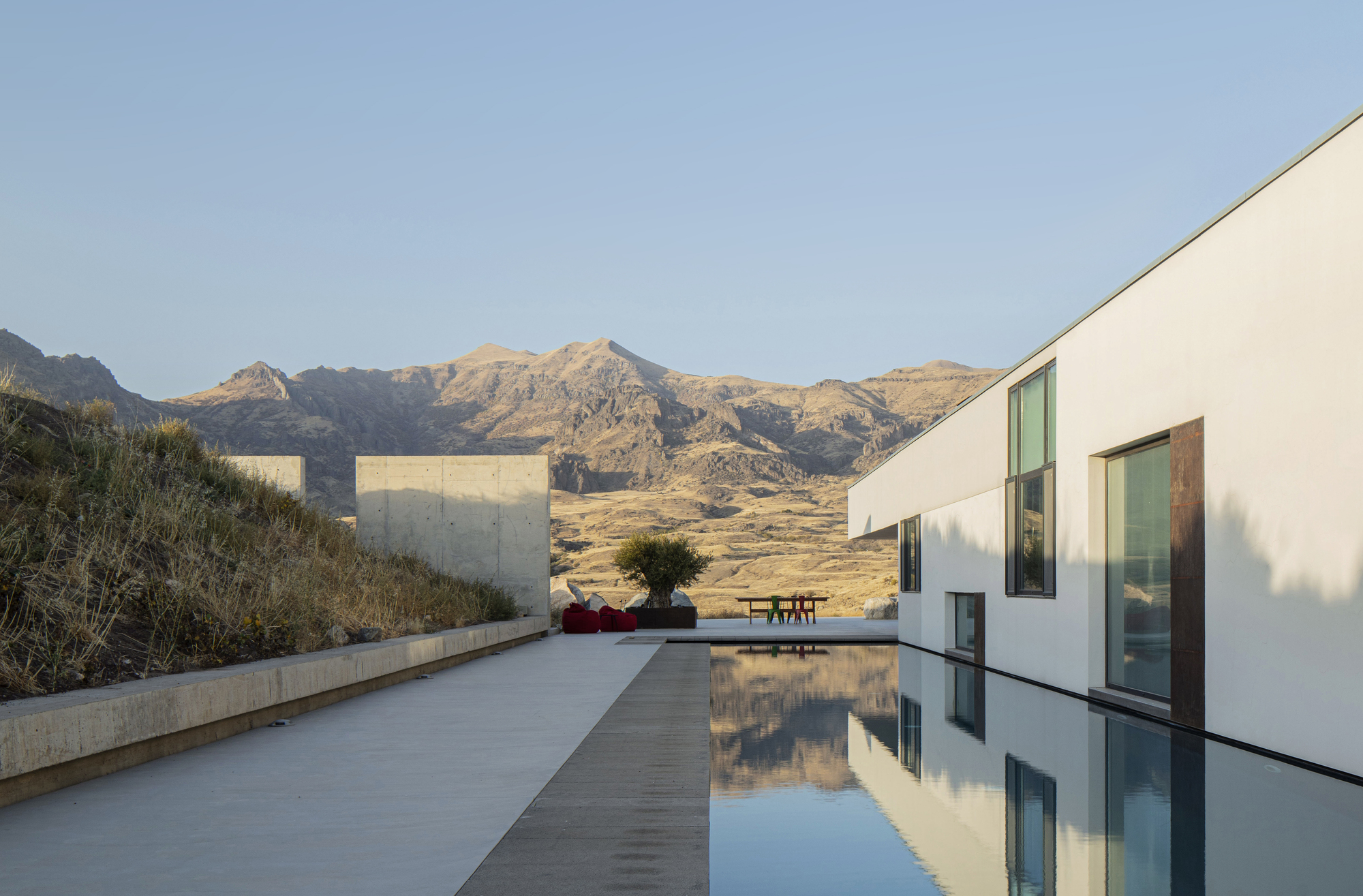 Concrete terrace with reflecting pool and white volumes framed by arid hills under evening light