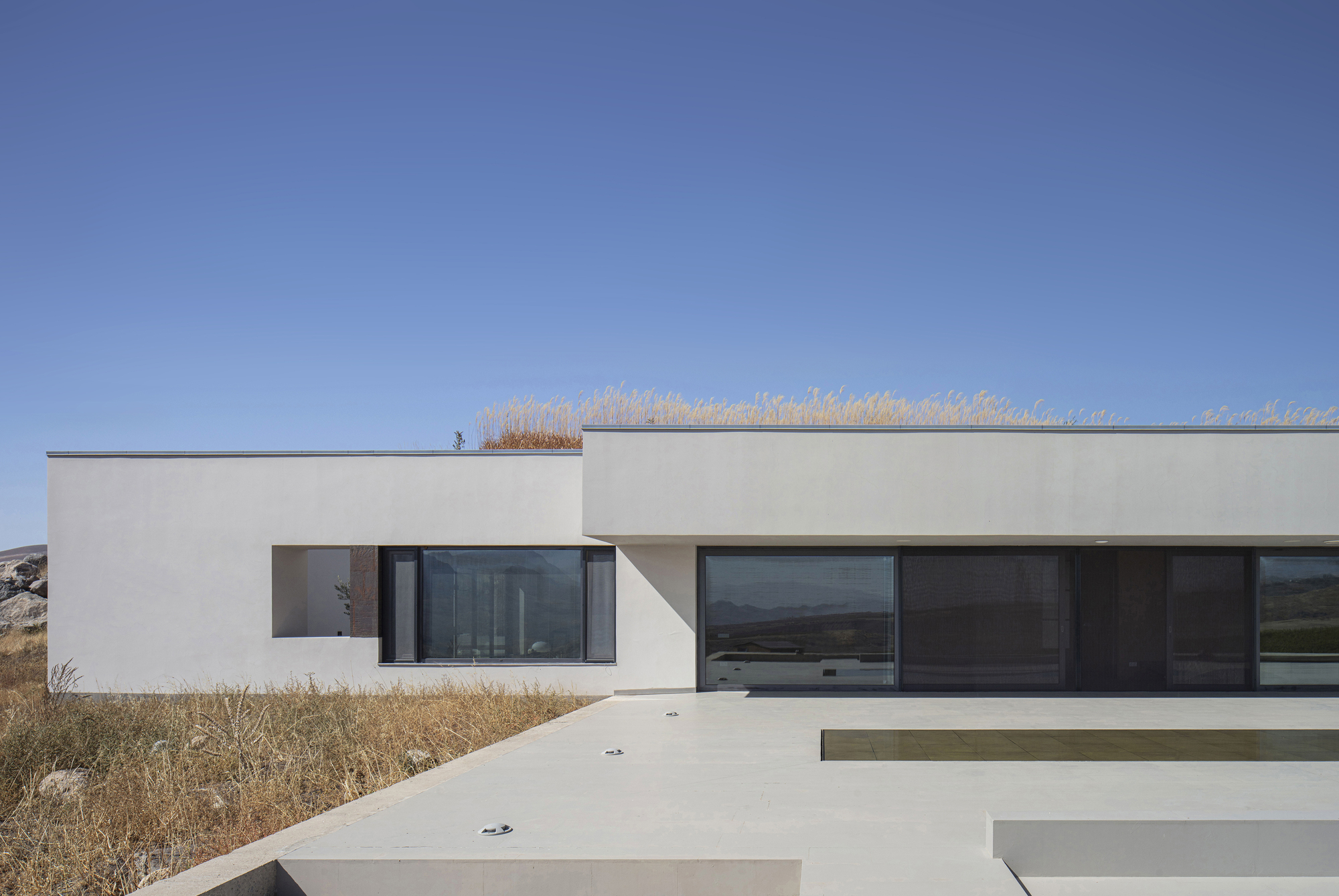 White stucco facade with horizontal windows and stepped concrete terraces against dry grasses