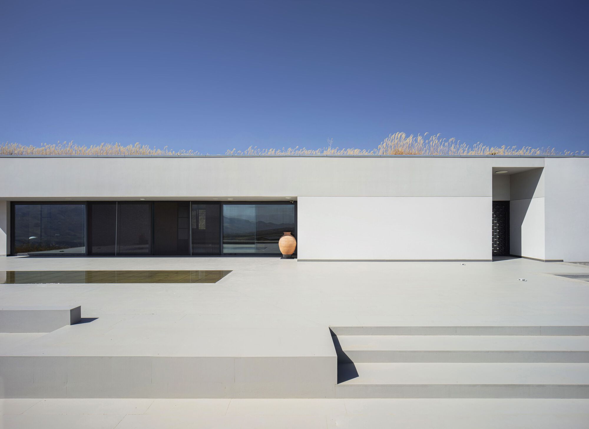 White rendered terrace with wide steps ascending to a horizontal window band under a clear blue sky