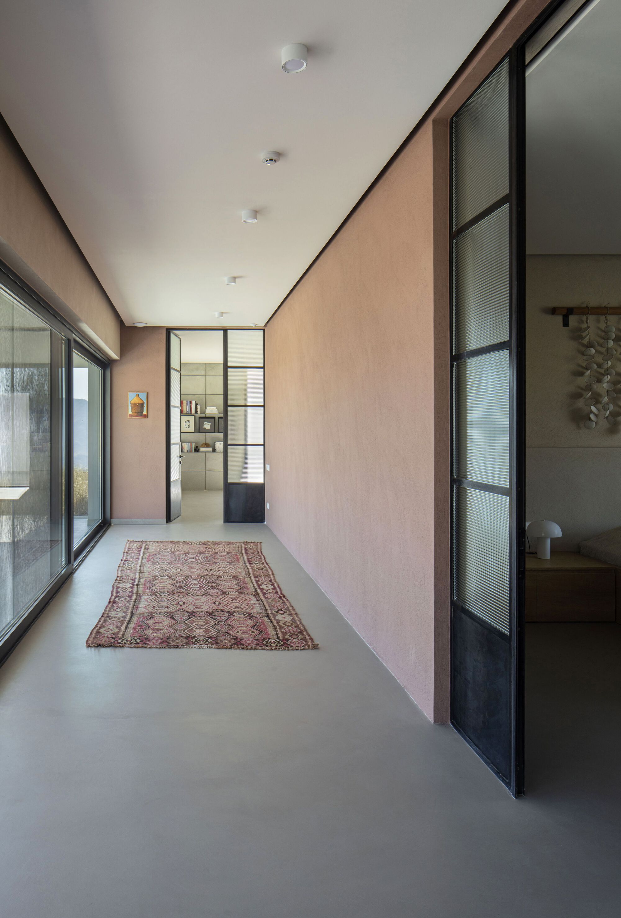 Corridor with pale plaster walls, steel-framed glass partitions, and a vintage rug on polished concrete flooring