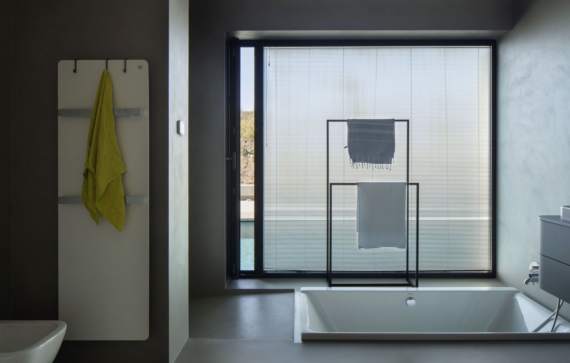 Bathroom with recessed tub beside a window fitted with translucent pleated blinds and a towel rack