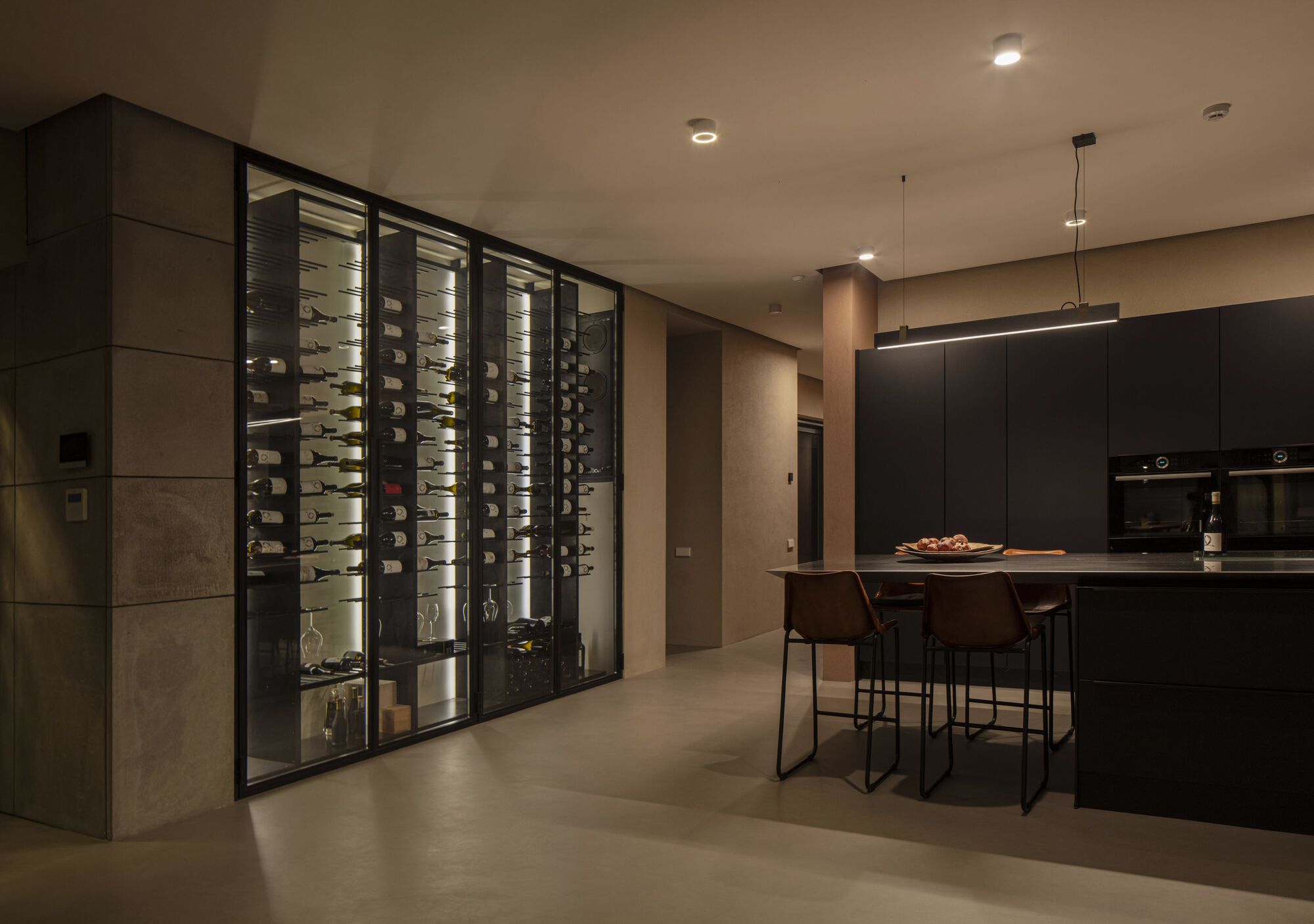 Kitchen with backlit wine storage wall and dark cabinetry under warm evening lighting