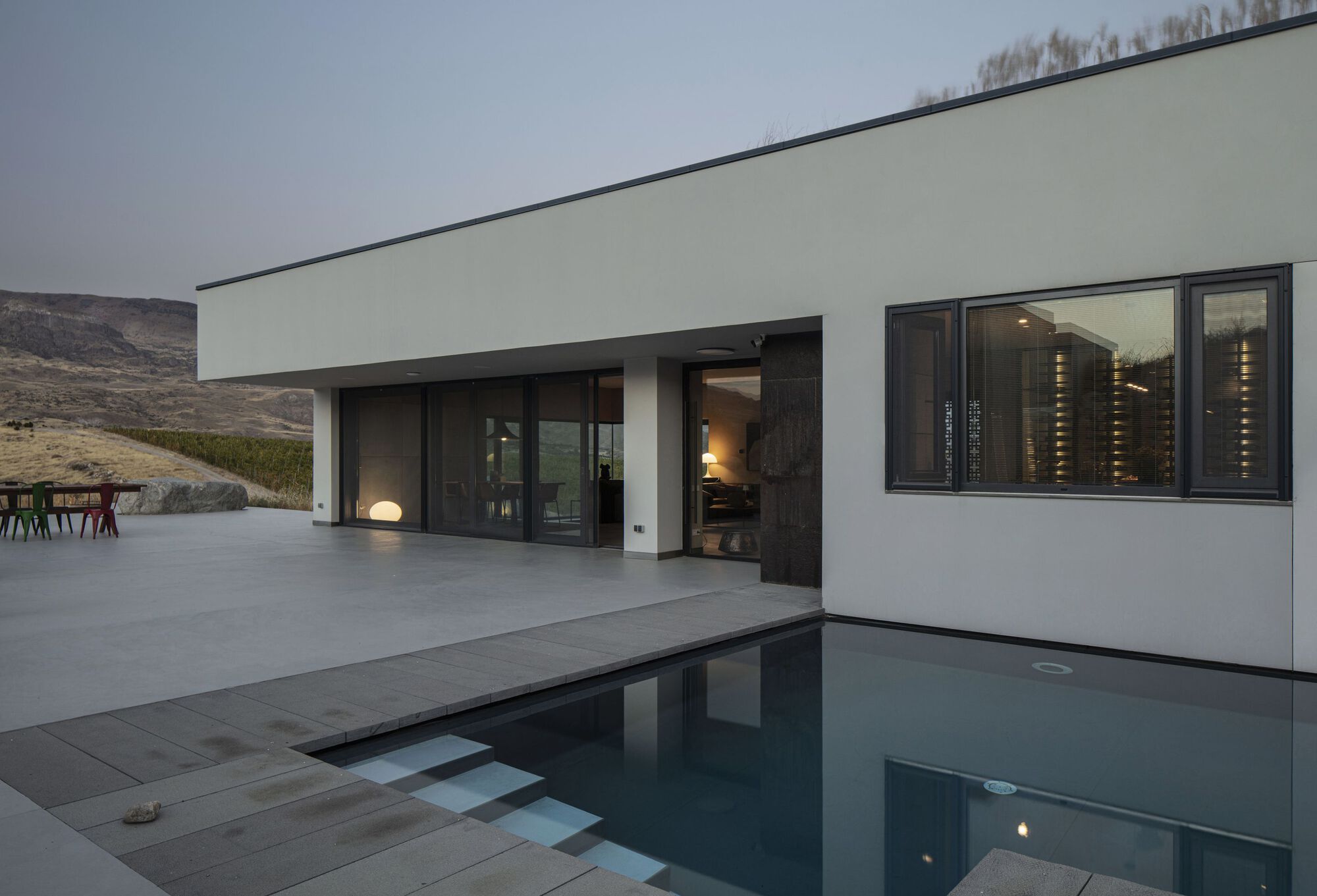Pool deck at dusk with still water reflecting the interior lights through sliding glass doors
