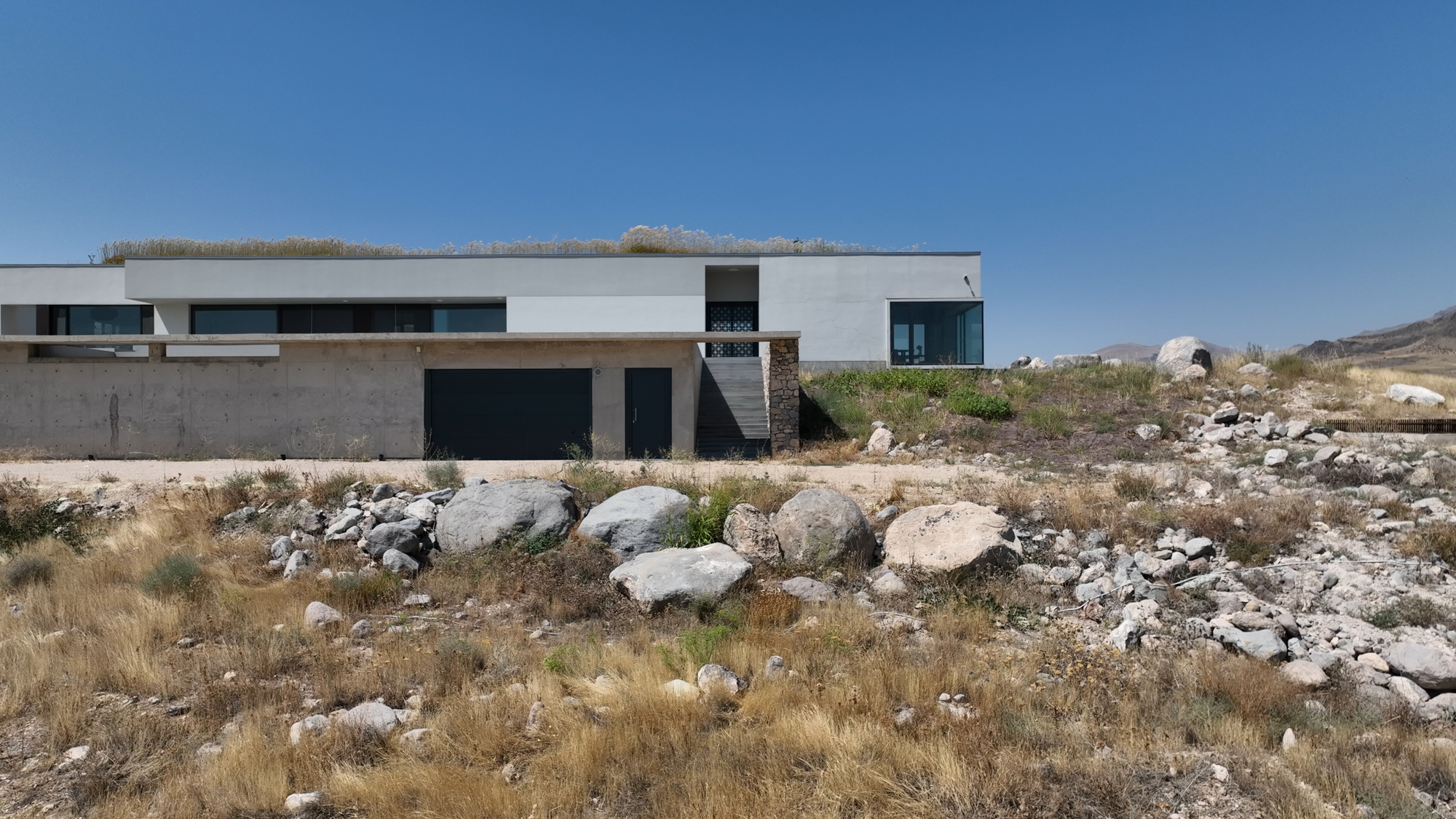 White horizontal volume with terrace roof set among rocky desert terrain under clear blue sky
