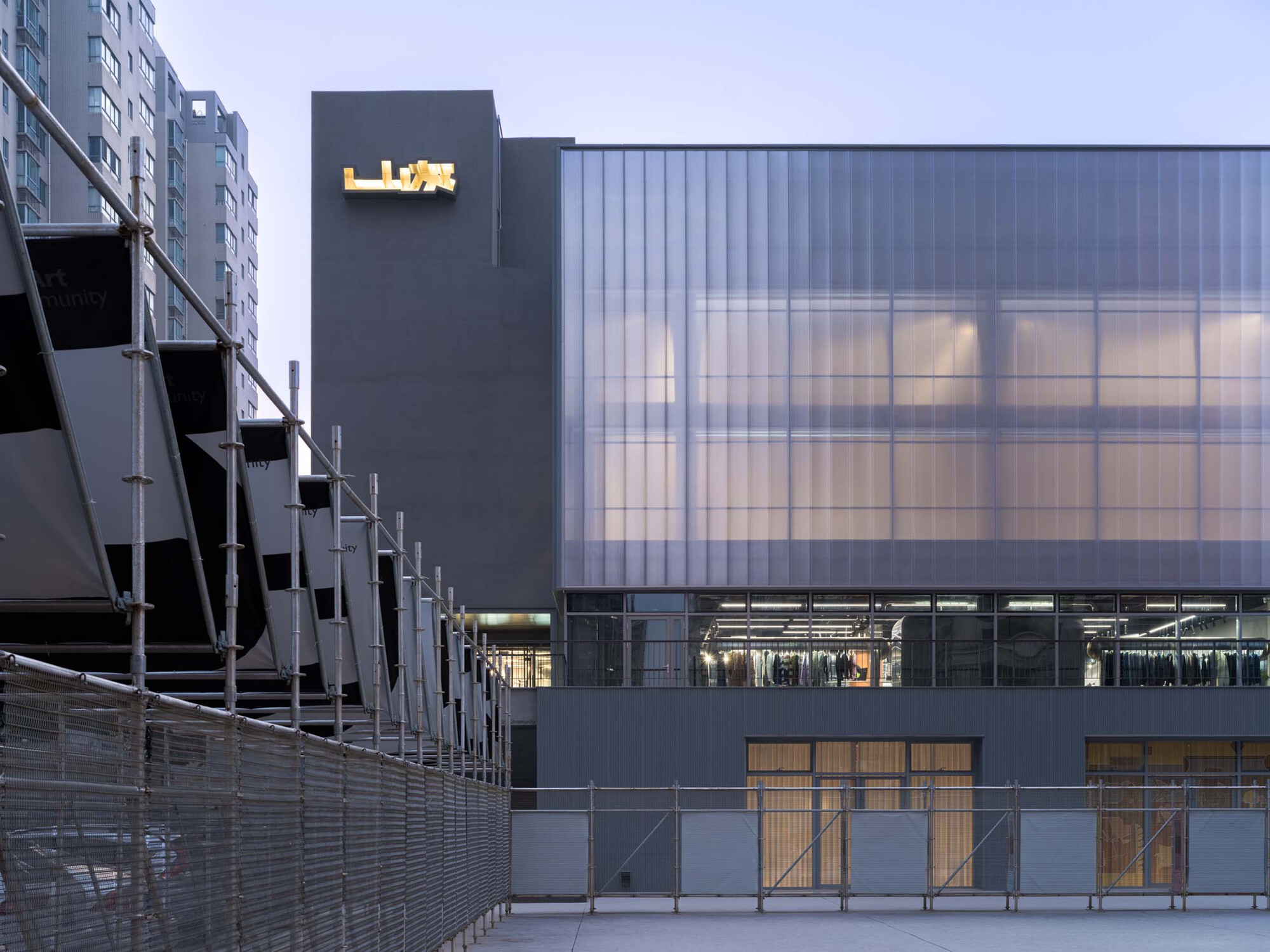 Translucent polycarbonate facade and projecting signage tower at twilight beside a residential block