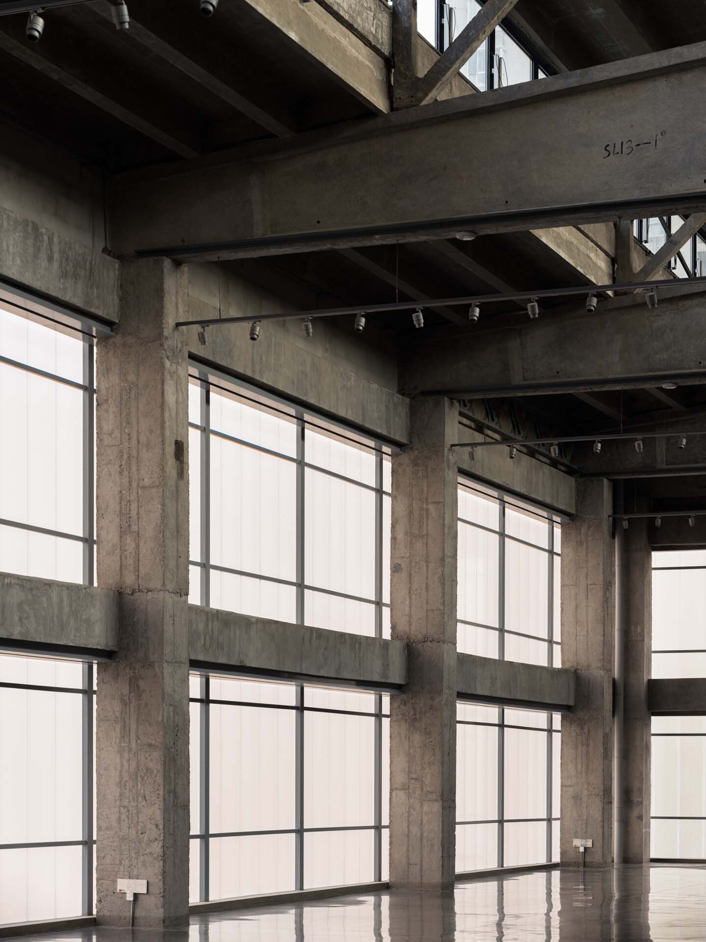 Interior concrete columns and exposed beams with tall gridded windows diffusing daylight