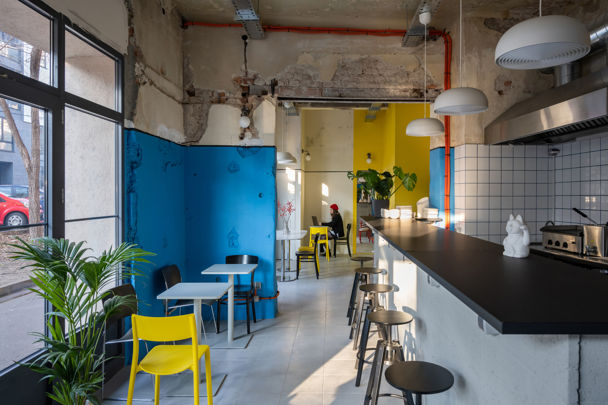 Cafe interior with exposed concrete ceiling, blue painted walls, white tile kitchen counter and yellow seating