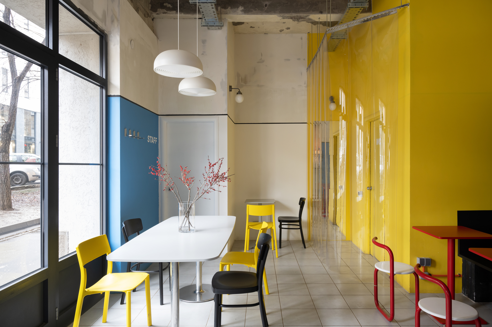 Seating area with white table and yellow translucent curtain beside blue wall and street-facing windows